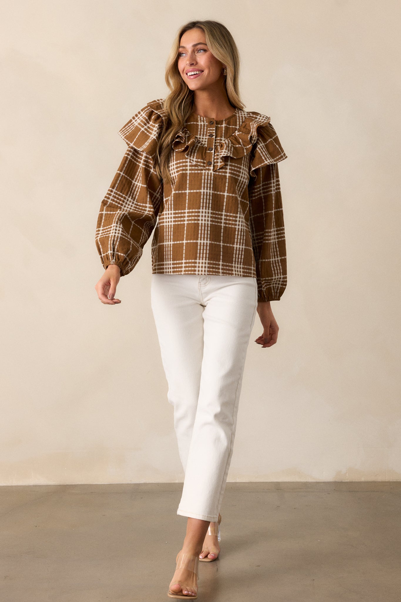 A full view of the mocha blouse, showcasing the rounded neckline with 4 functional buttons, the plaid pattern, and long puff sleeves with flutter detailing.