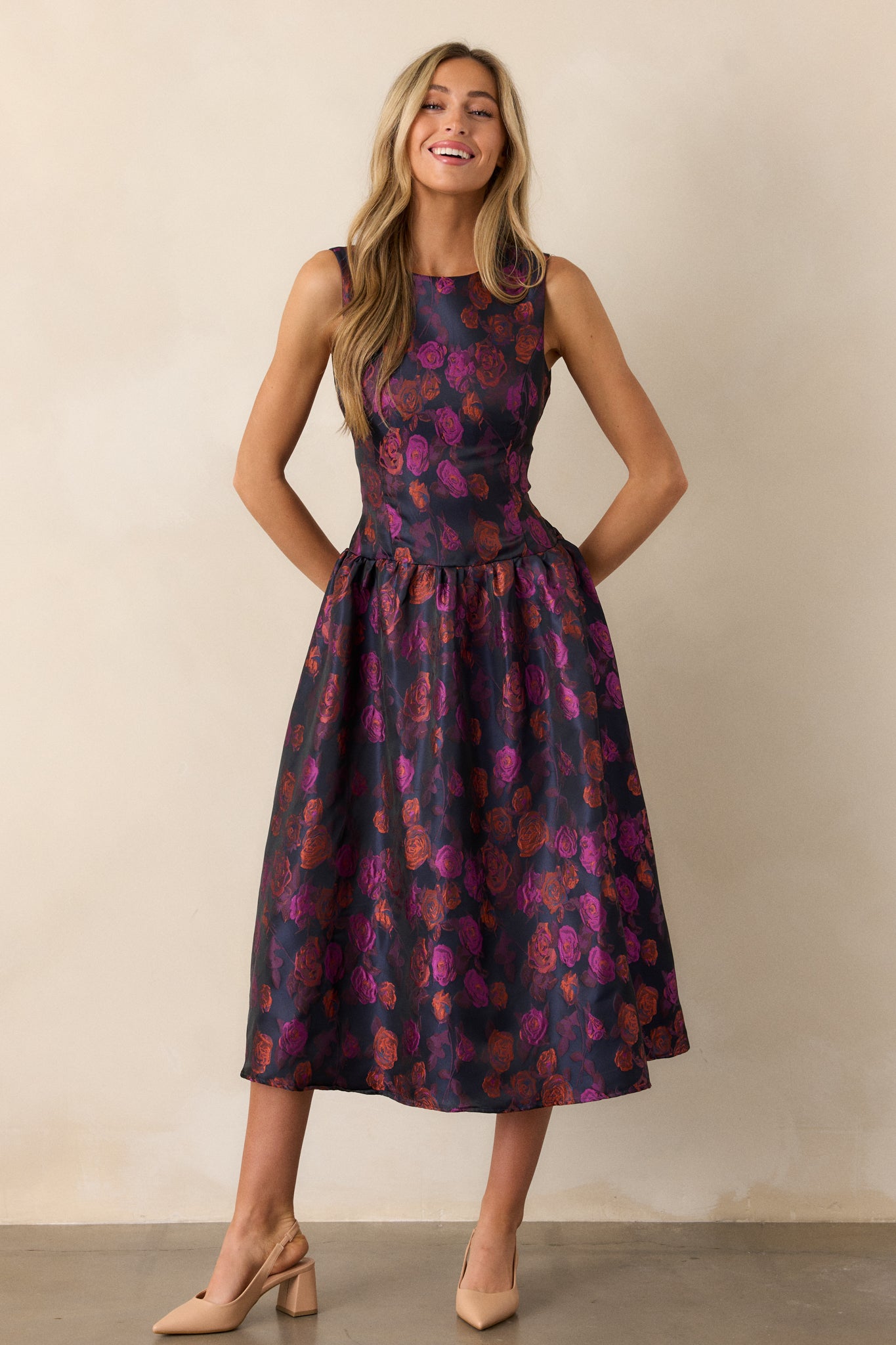 A purple dress featuring a vibrant floral design, with a high rounded neckline and sleeveless cut, flowing elegantly to a midi length.