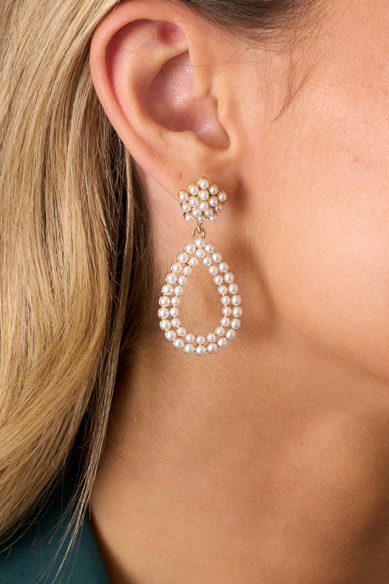 A pair of ivory earrings featuring a cluster of faux pearls as a stud, leading to a teardrop dangle embellished with additional faux pearls and gold hardware.