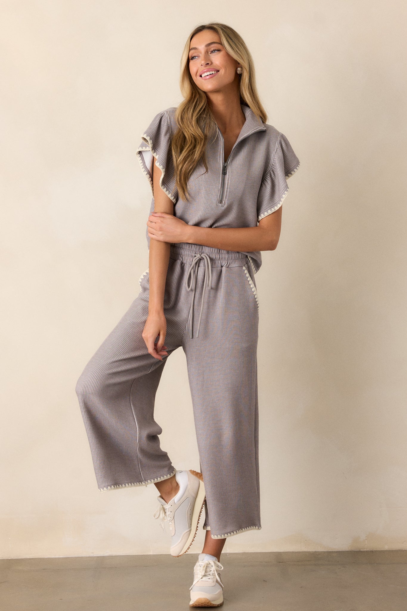 Full body of these grey pants that feature an elastic waistband, an optional waist drawstring, an ivory ruffle trim, functional hip pockets, a soft stitched material and a wide leg