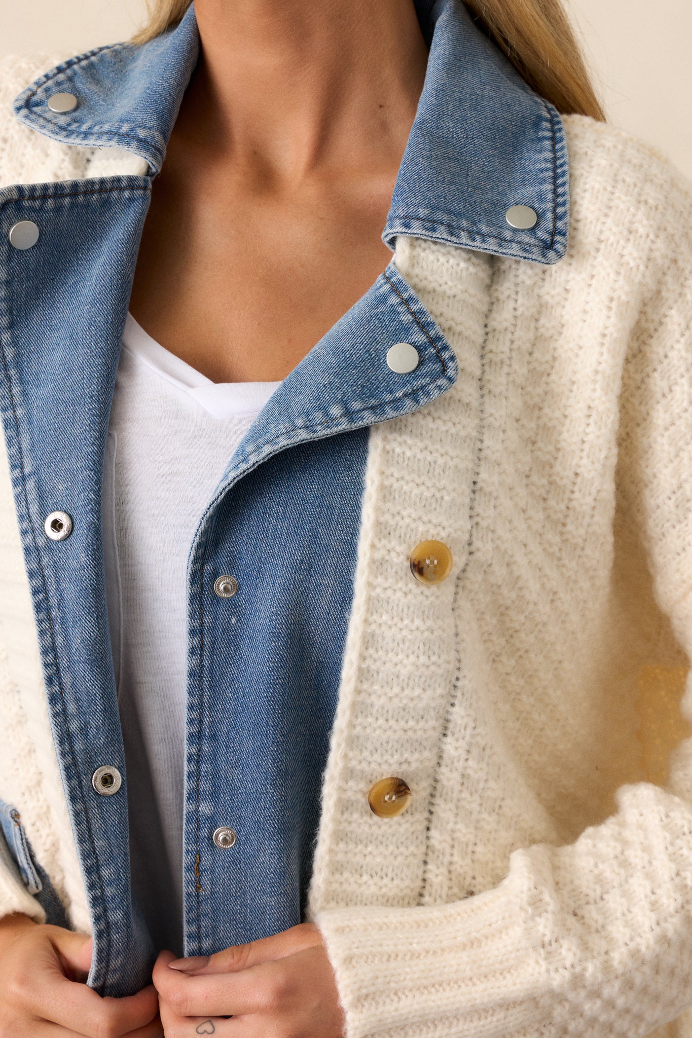 A close-up of the brown detail buttons on the ivory knit overlay, showing the texture of both the knit fabric and the blue denim pockets.