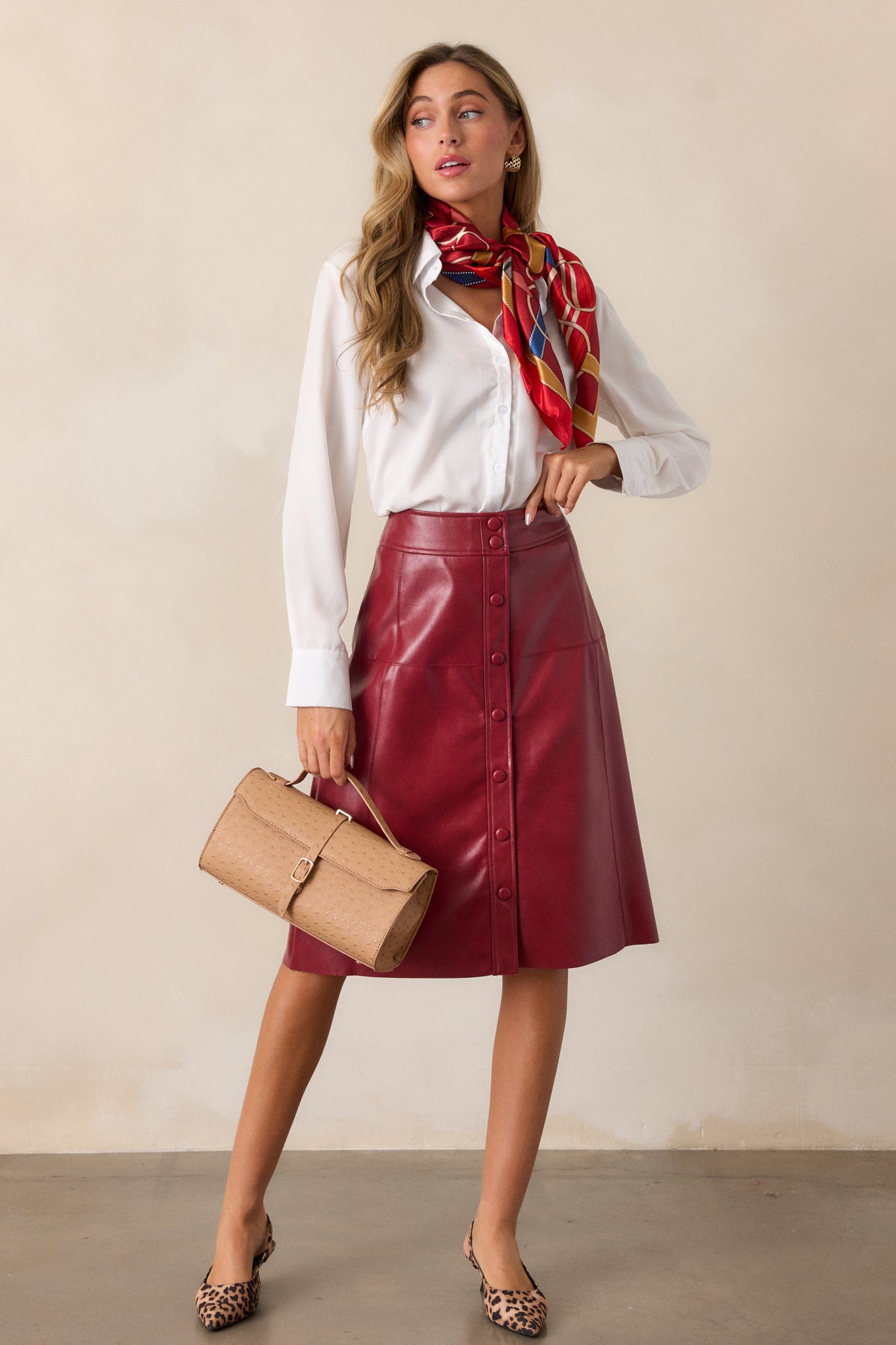 Full front view of the burgundy midi skirt, featuring a sleek faux leather material and a functional snap button front.