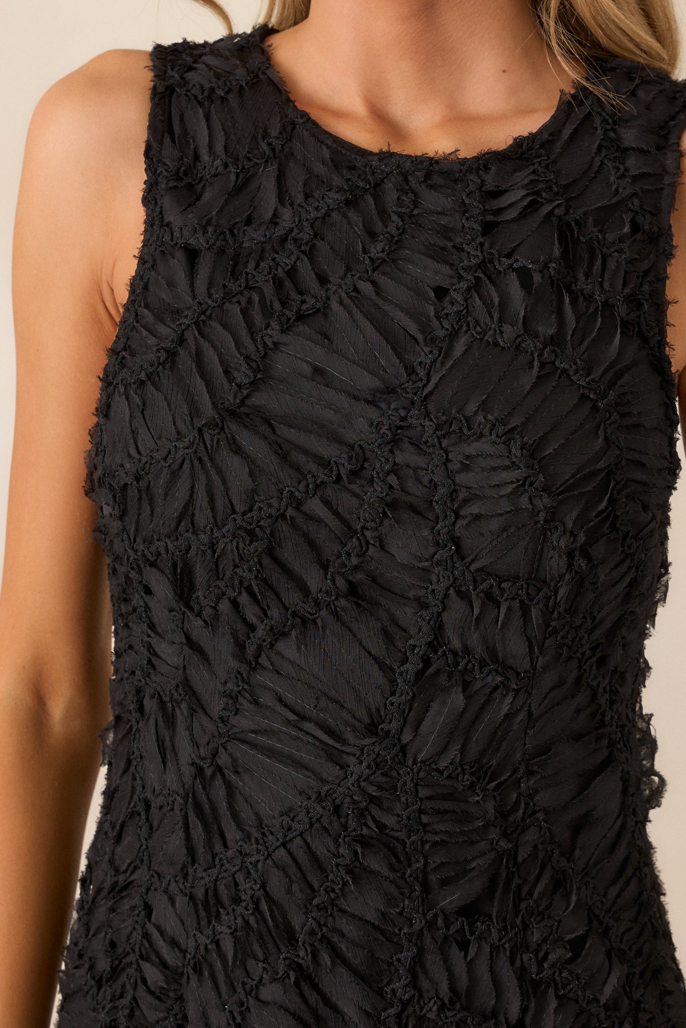 A close-up of the dress’s textured fabric, showing the intricate detailing and rounded neckline with the sleeveless design.