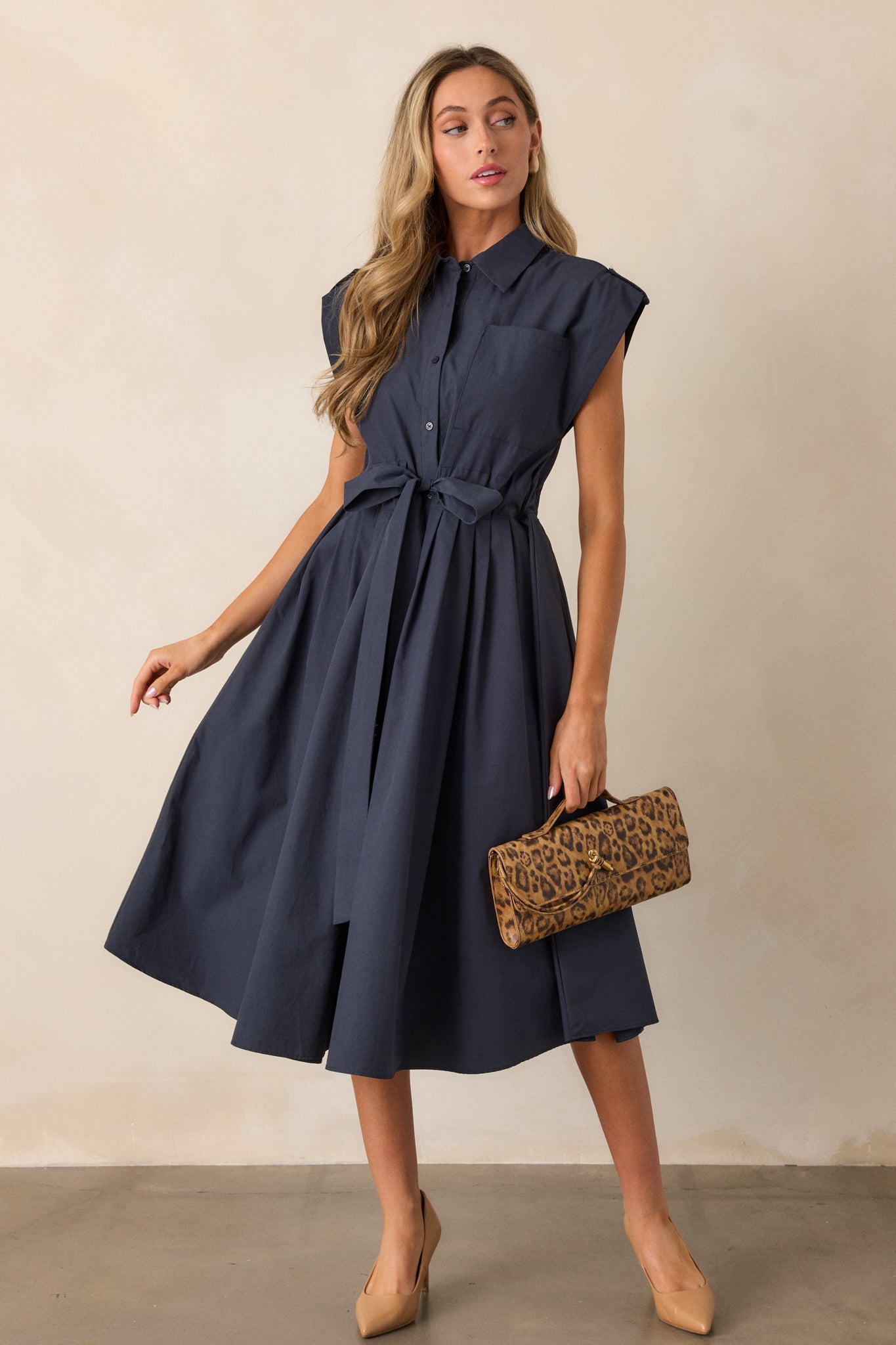 A front view of the navy dress with the functional breast pocket clearly visible, showcasing the button detailing along the front and the relaxed fit of the cap sleeves.