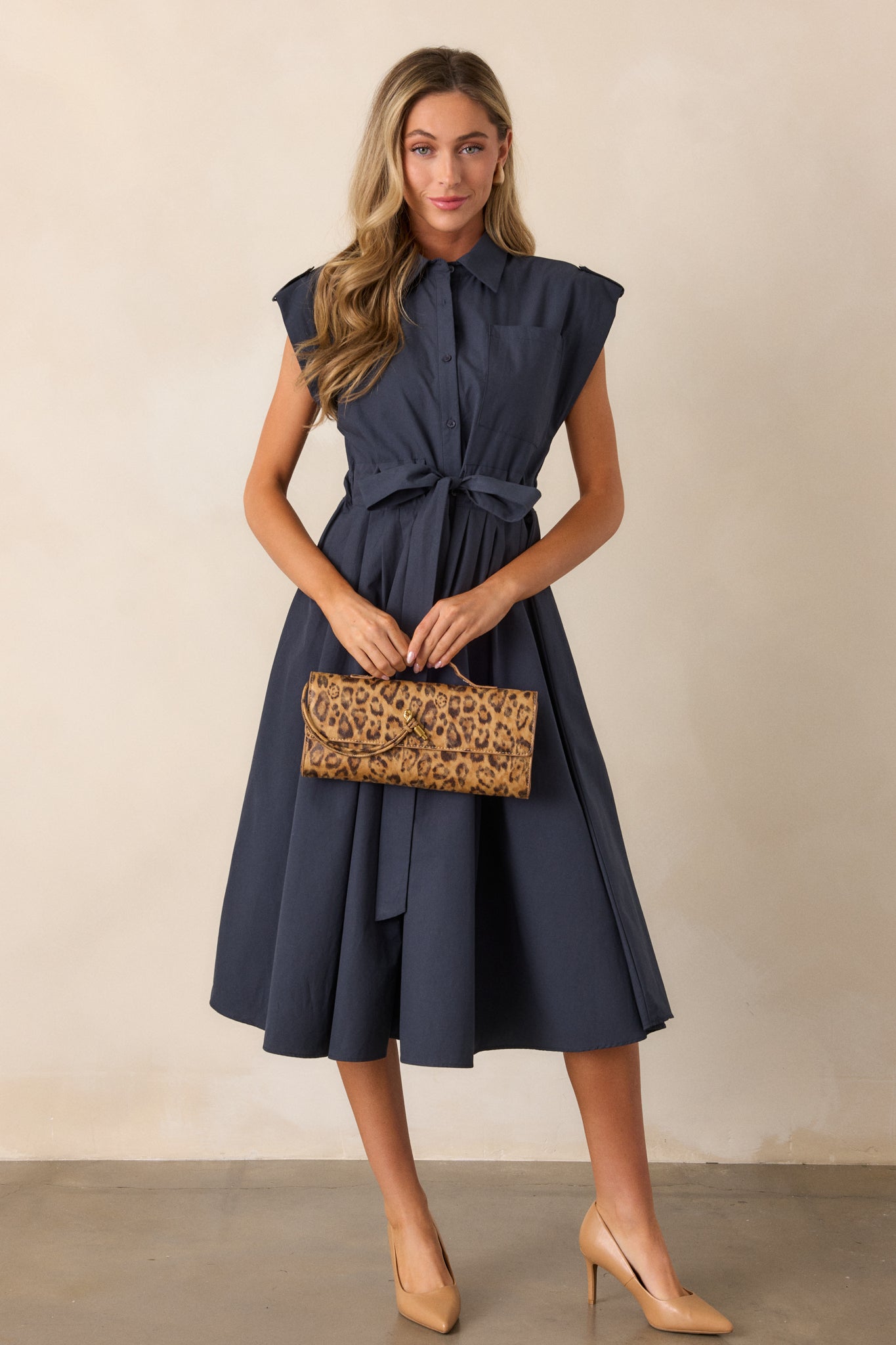 A full-length view of the navy dress featuring a collared neckline and functional button front, complemented by a self-tie belted waist, creating a flattering silhouette.