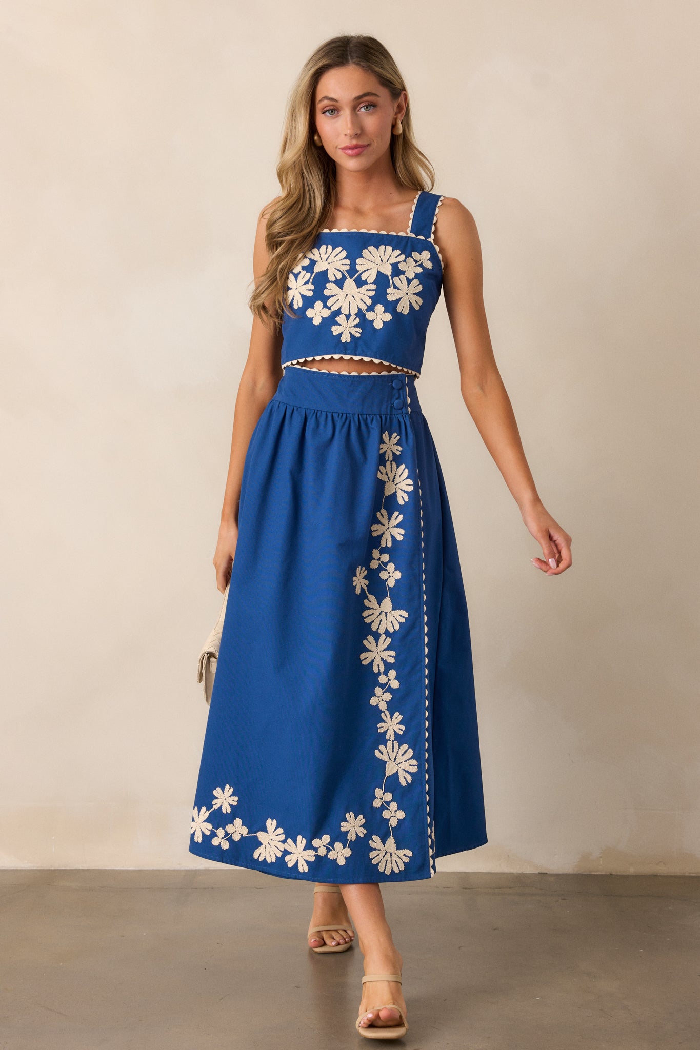 Full view of the blue top, highlighting the ivory embroidered floral design and squared neckline against a light background.