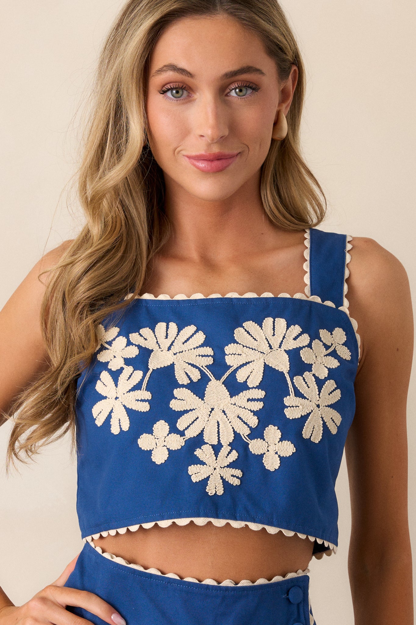 Front view of the blue top emphasizing the squared neckline and full button back closure, presented on a neutral backdrop.