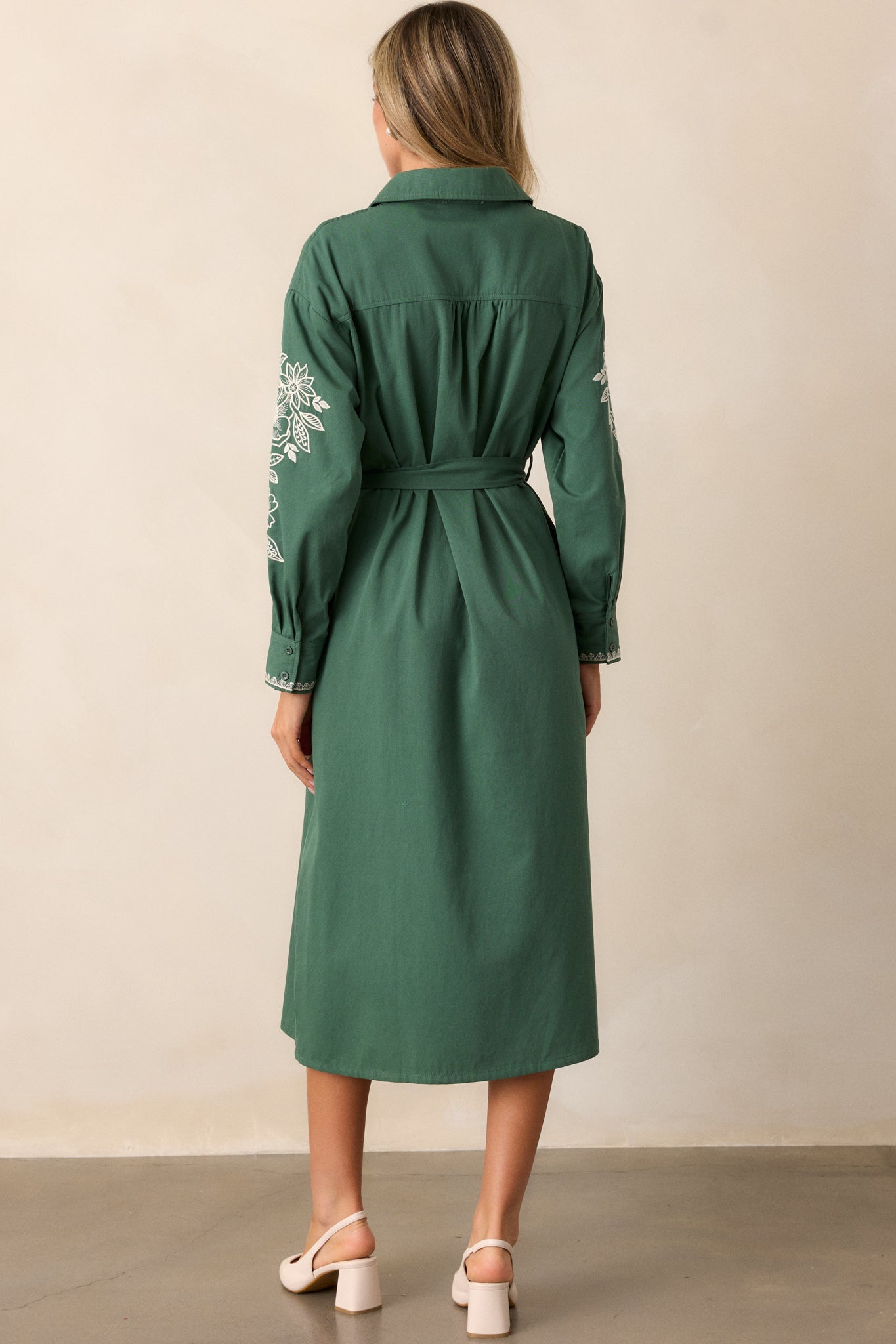 Back view of the dress, showcasing the simple, elegant flow of the material, collared neckline, and the structure of the long sleeves.