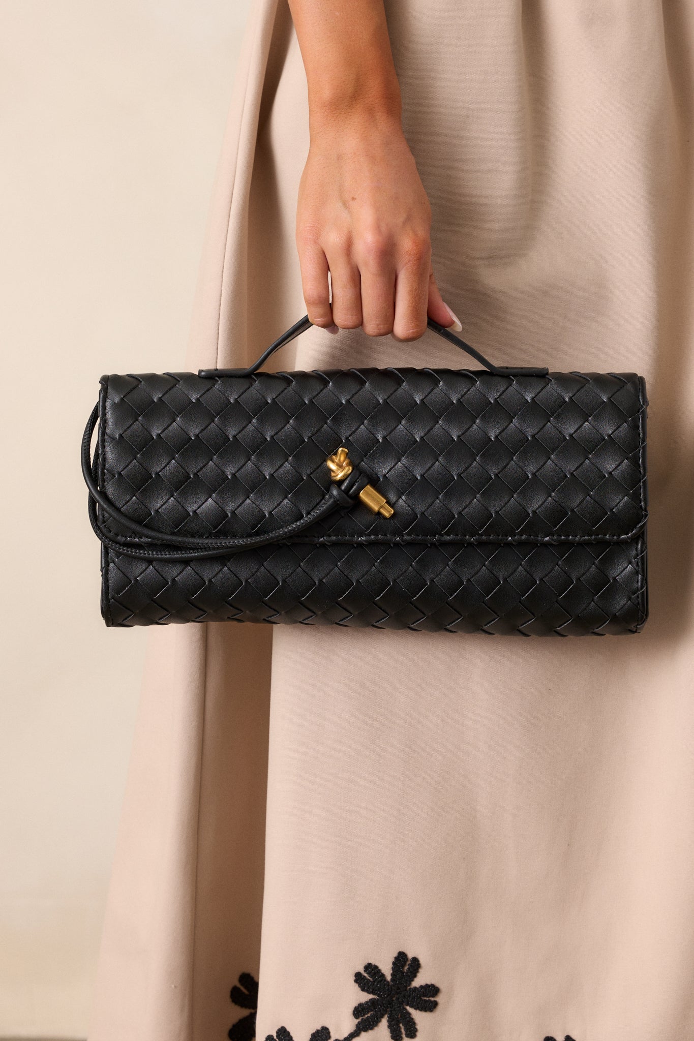 A full view of the black handbag, featuring its rectangular shape, black handle on top, and gold accent front piece.