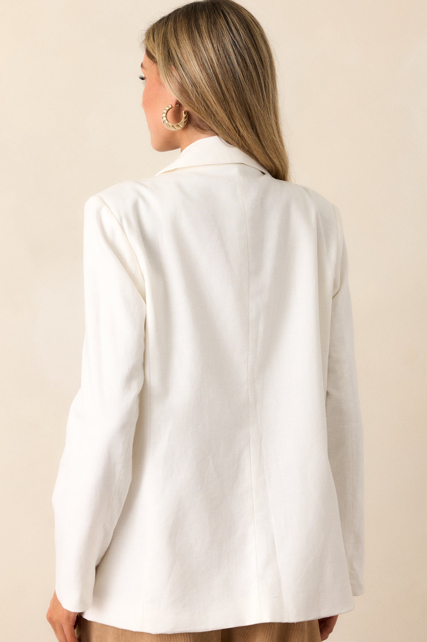 Back view of a white blazer highlighting the clean lines of the back, padded shoulders, and the full length of the long sleeves.