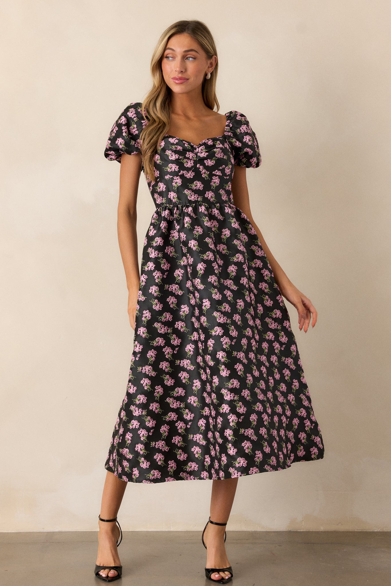 A black midi dress showcasing a pink floral jacquard design, featuring a sweetheart neckline and puff sleeves, complemented by an elegant A-line silhouette.