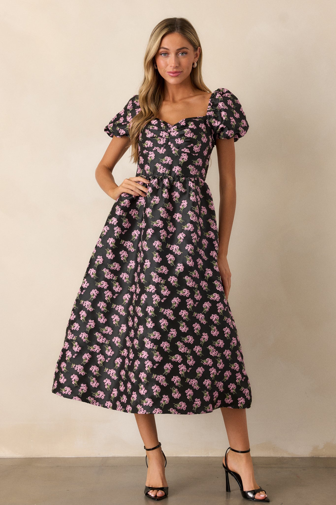 The black midi dress displayed in full, highlighting the fitted bodice and flared skirt, with a vibrant pink floral pattern adding a touch of femininity.