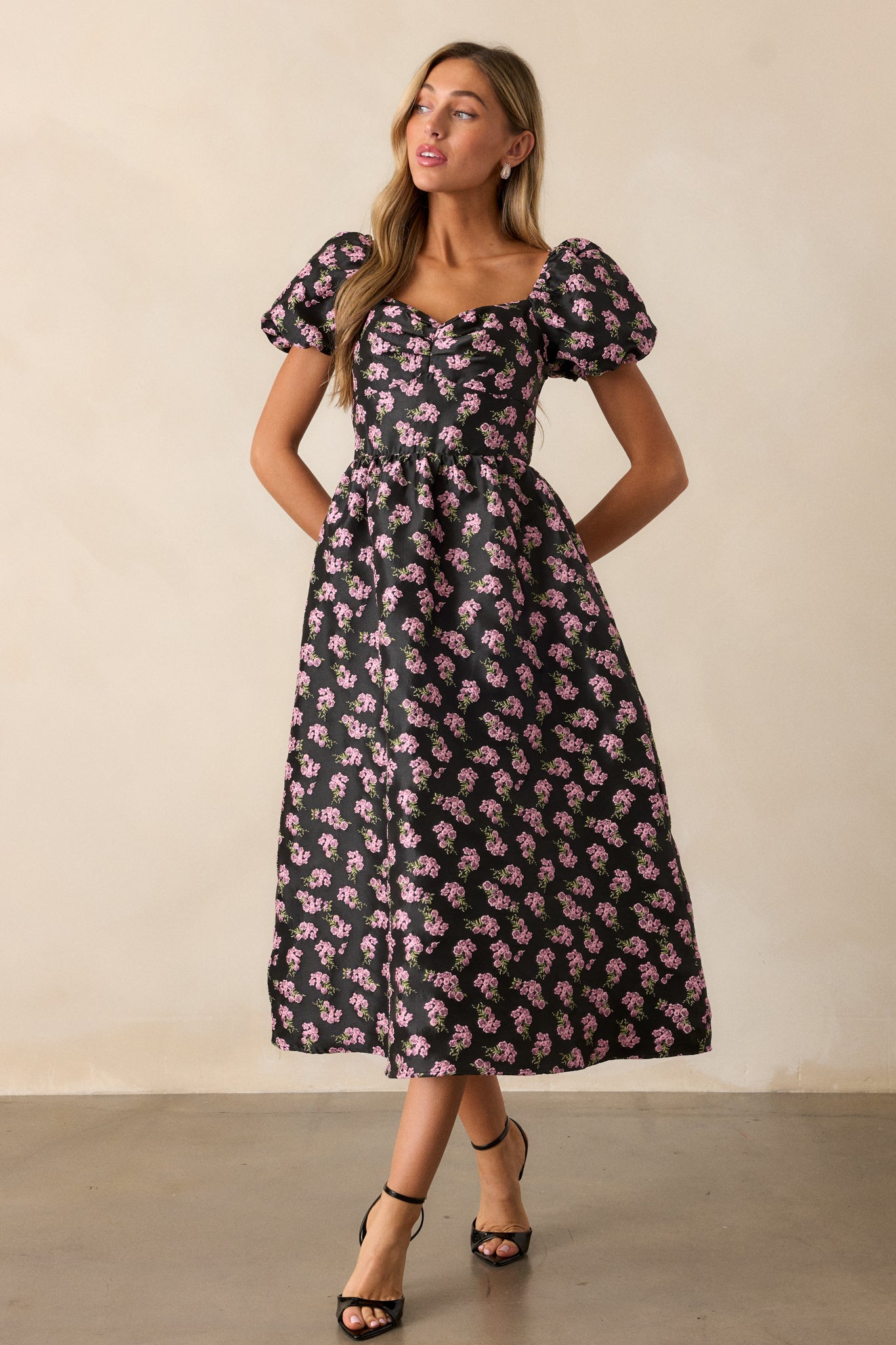 A full-body shot of the black midi dress, focusing on the beautiful pink floral jacquard design and the elegant puff sleeves that enhance the overall look.