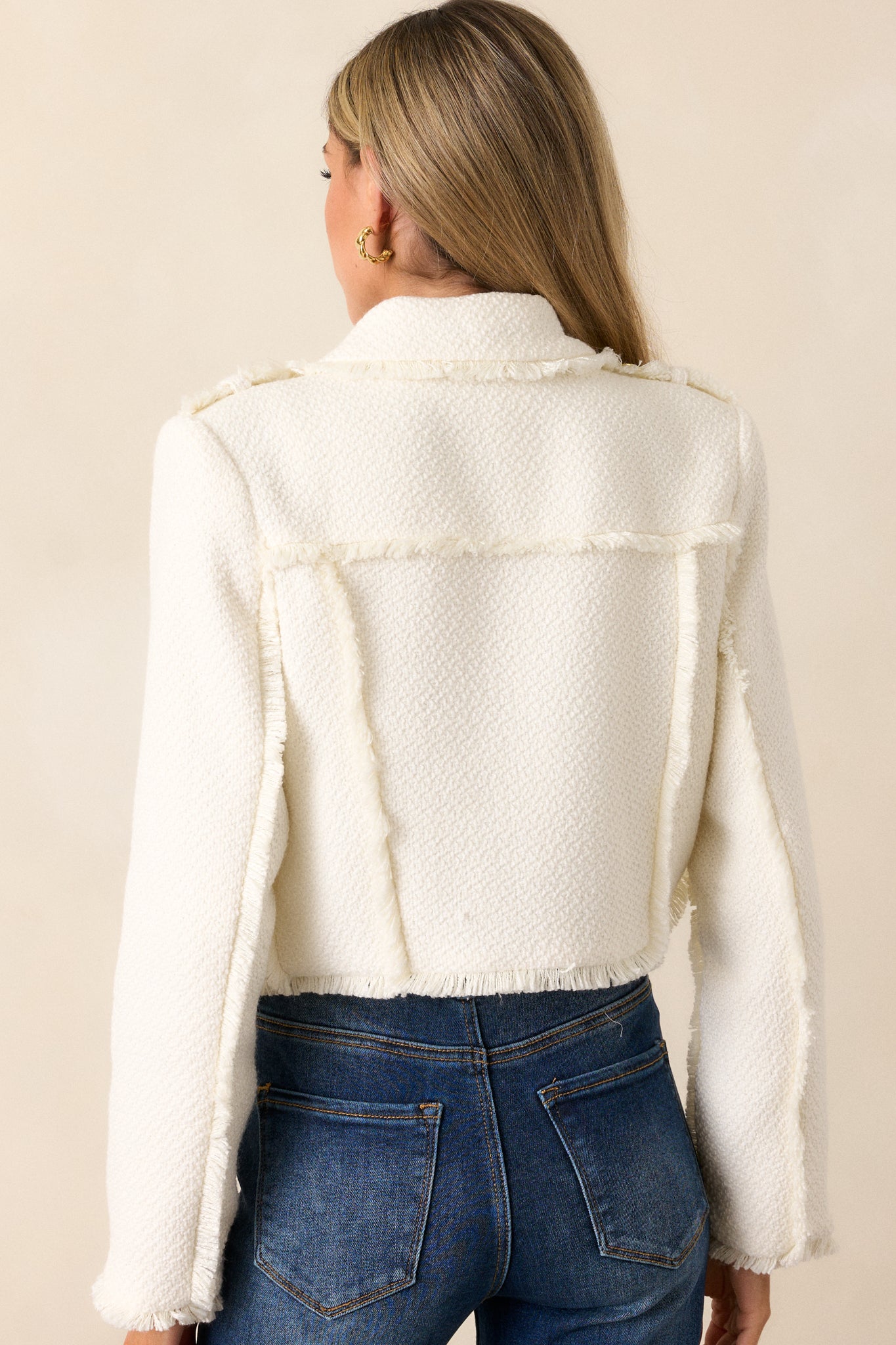 Rear view of the white cropped blazer, focusing on the clean, structured lines across the back and the raw hem at the waist.