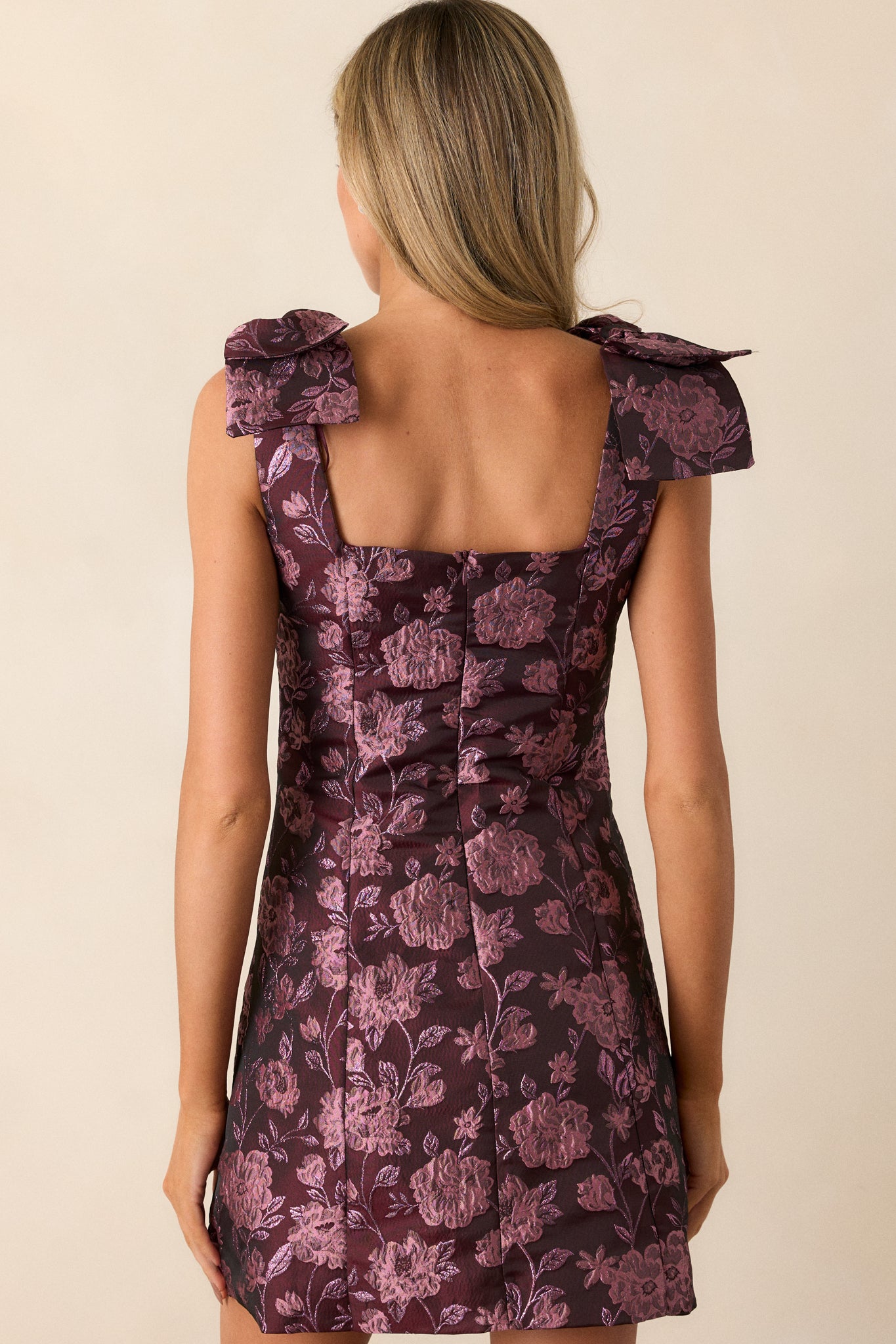 The back of the mini dress, featuring the purple floral jacquard fabric, sleeveless straps with bows, and a fitted bodice with an invisible zipper down the center.