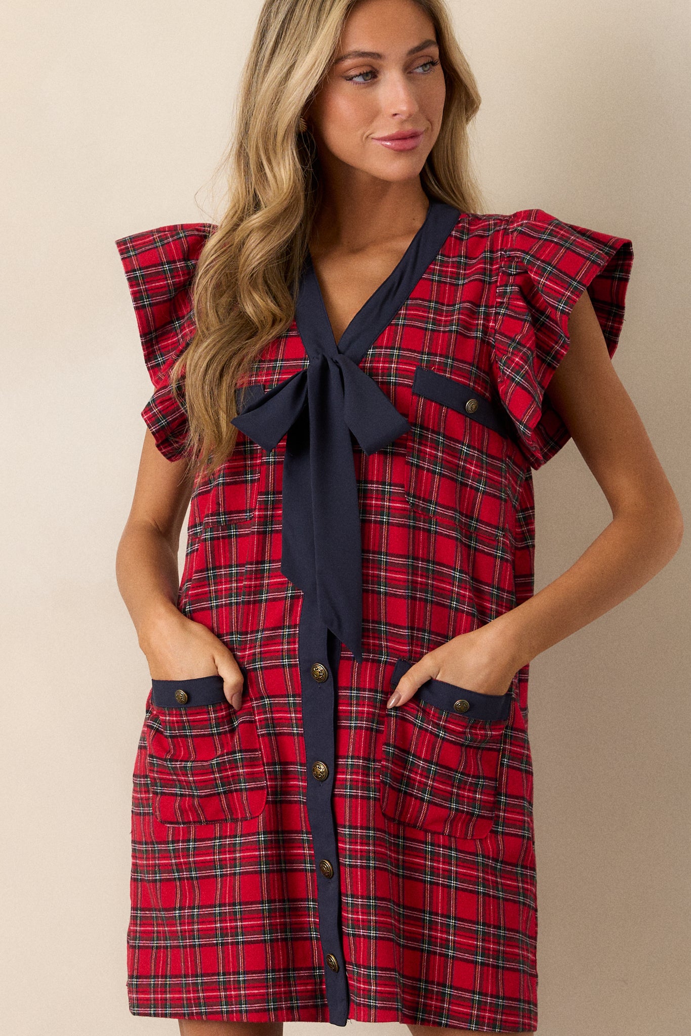 Close-up of the v-neckline of the plaid mini dress, highlighting the navy bow detail and antique gold buttons.