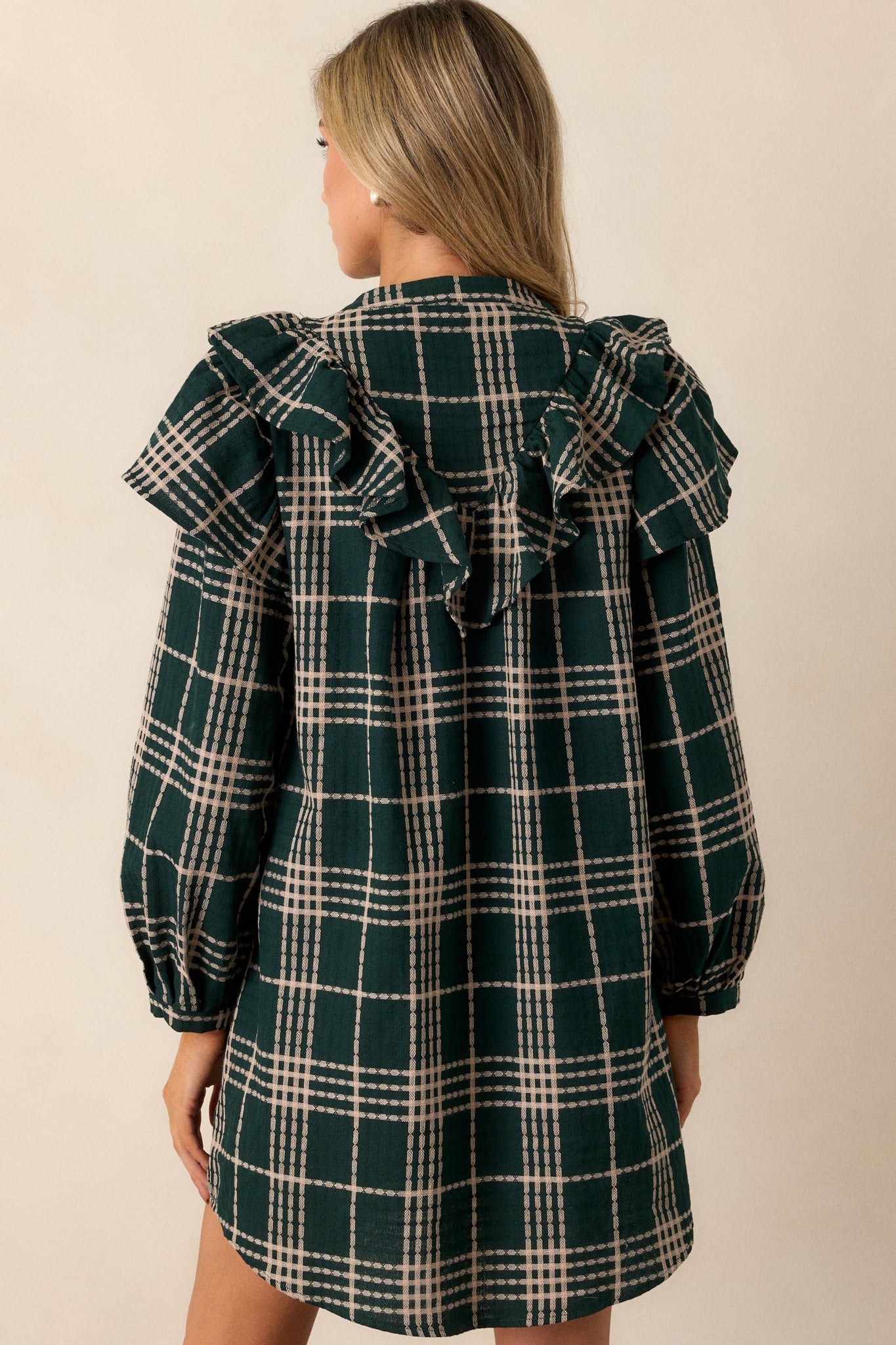 A back view of the mini dress showcasing the smooth flow of the plaid print and the long sleeves, with the ruffled yoke detail extending across the shoulders.