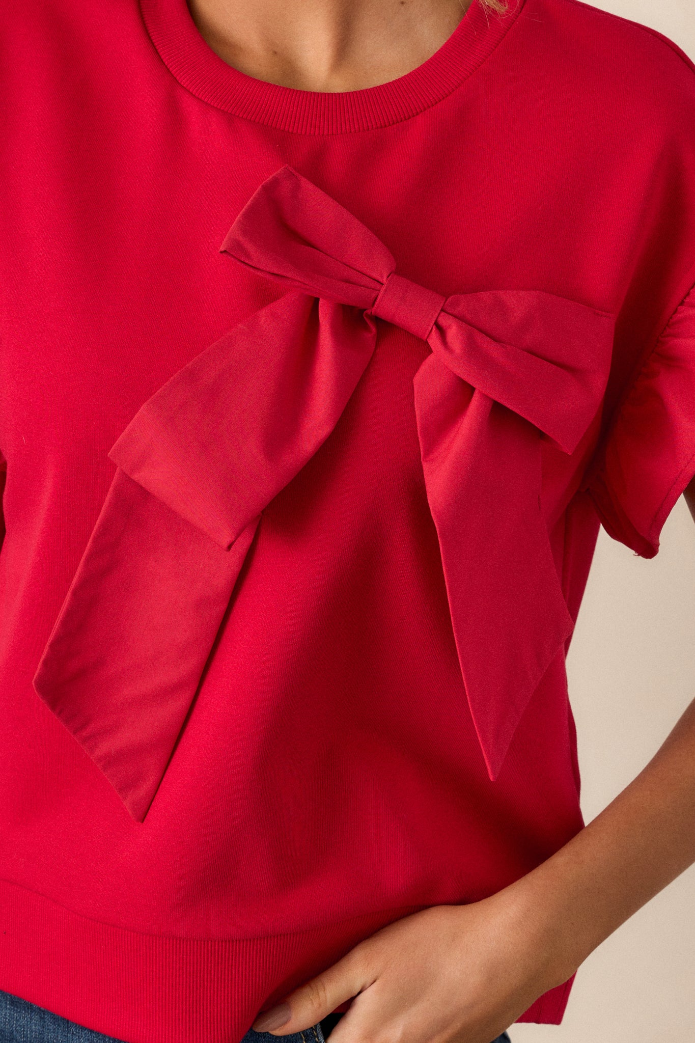 Close-up of the bow accent on the front of the red top, highlighting the knot and smooth fabric.