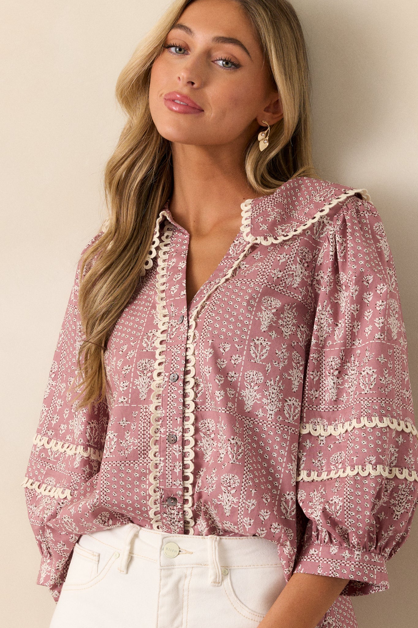 This dusty pink blouse features a collared v-neckline, button up front, small scalloped hemming, a beautiful floral pattern, and 3/4 puff sleeves with scalloped detailing.