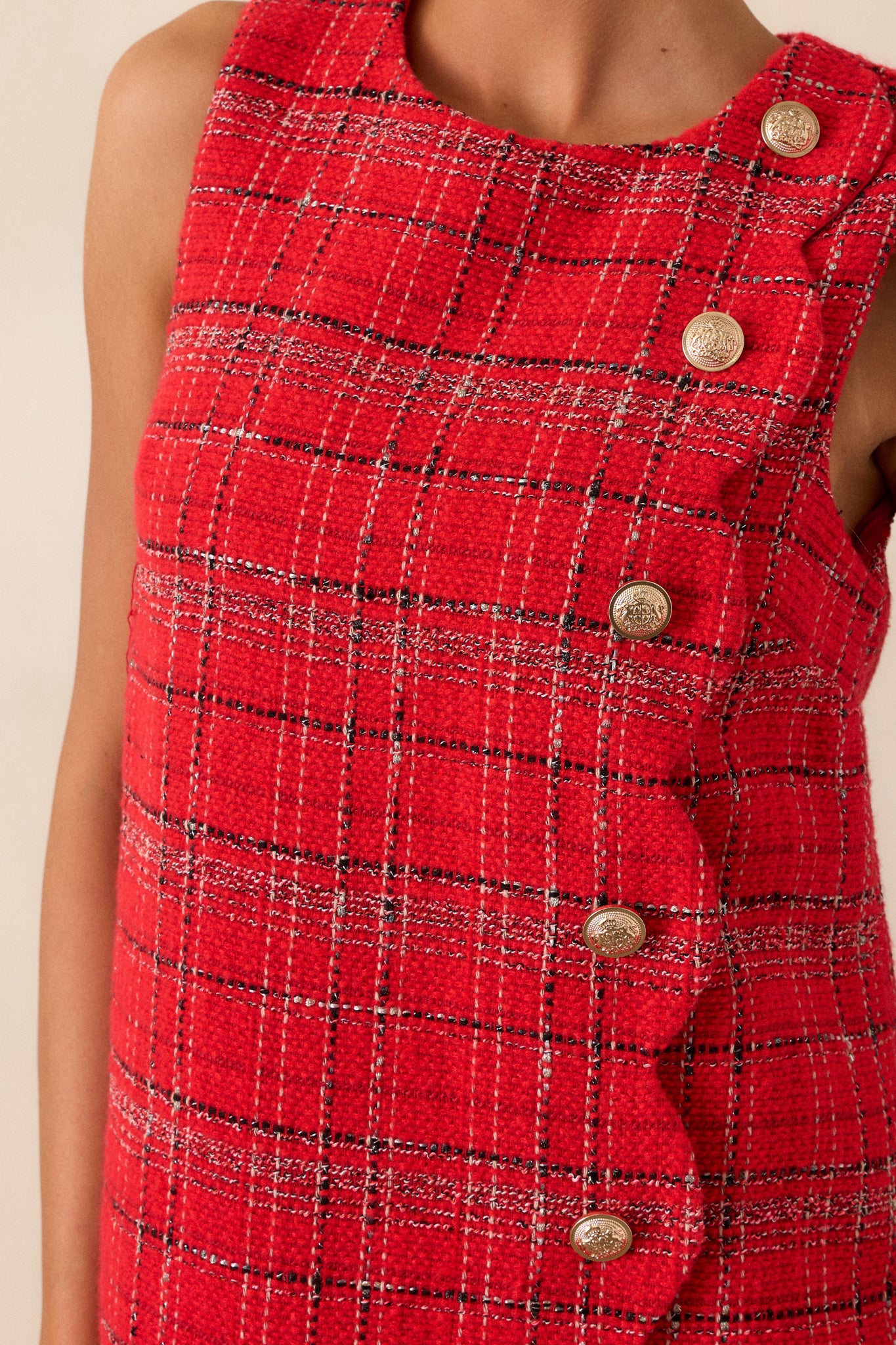 Close-up of the decorative gold-embellished buttons on the front of the red dress, highlighting the intricate scalloped hem design.