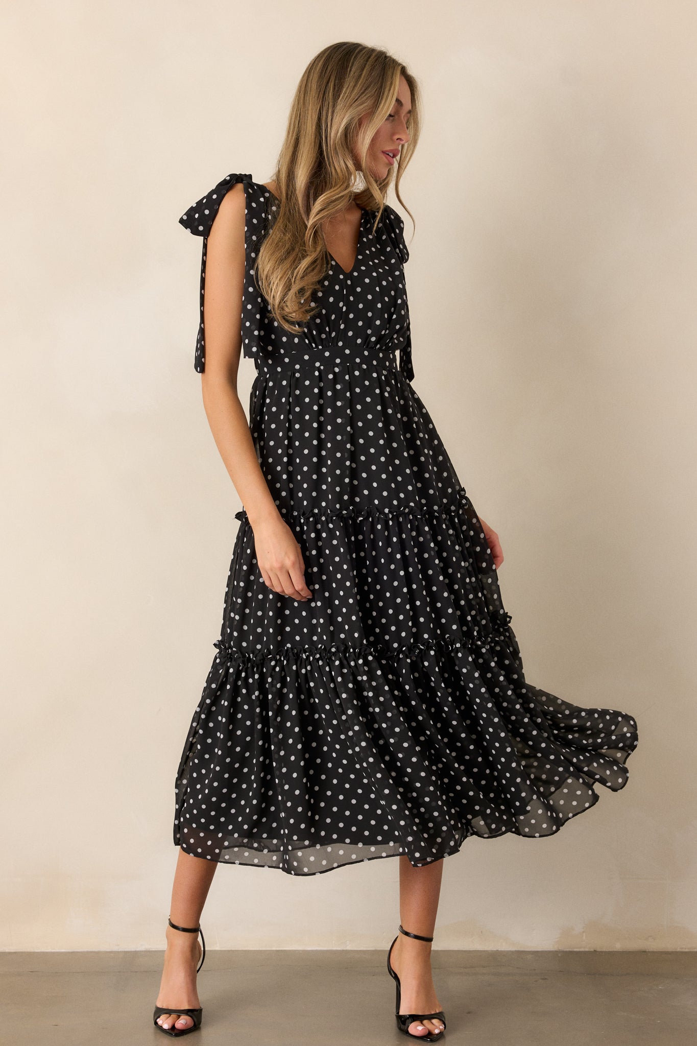 Side view of the black dress, highlighting the tiered skirt with ruffled hems, the v-neckline, and the self-tie sleeves, with the polka dot pattern visible.