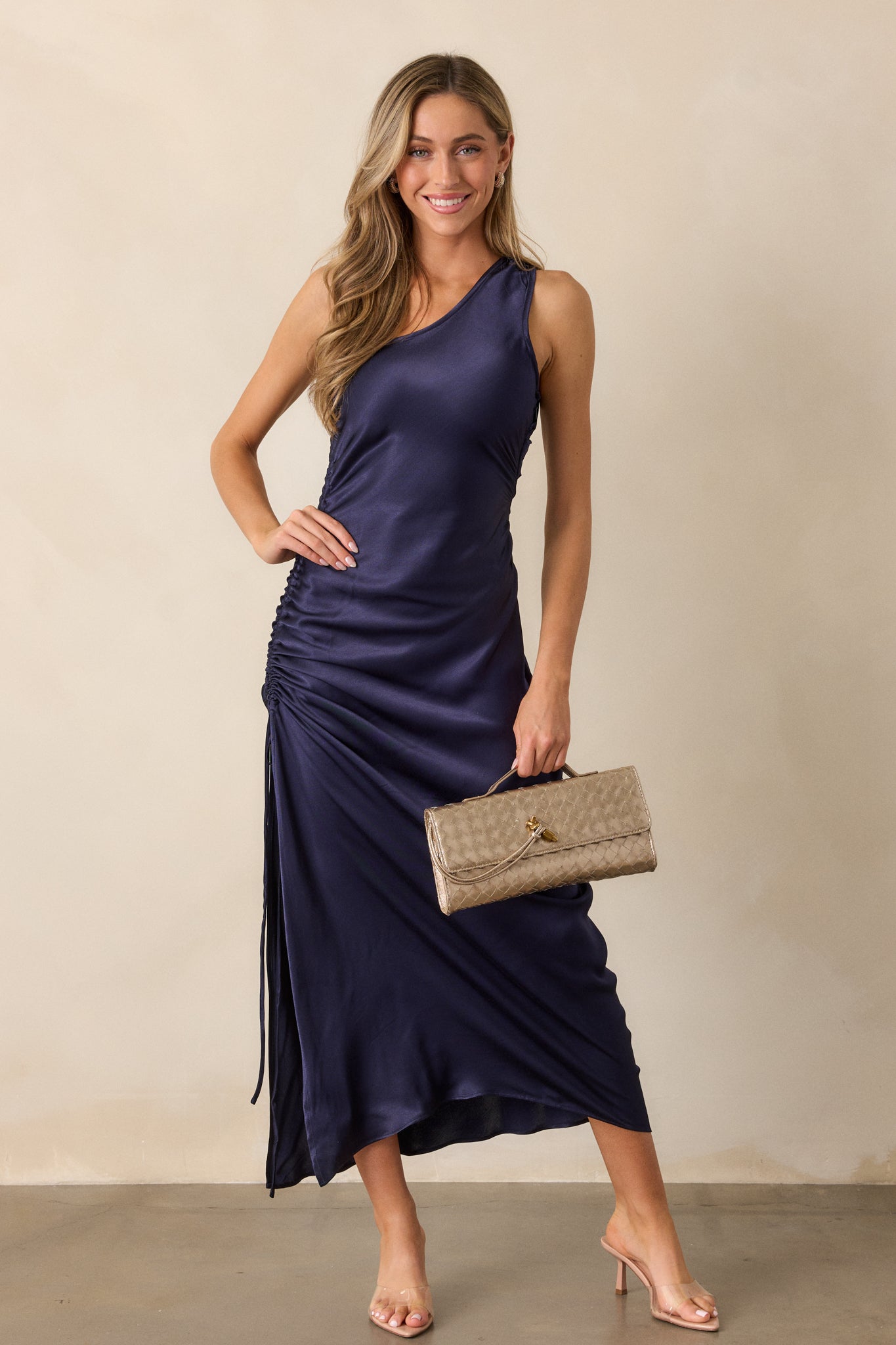 Full front view of the midnight blue dress, showcasing the one-shoulder neckline, fitted design, and ruched side detailing leading to a side slit.