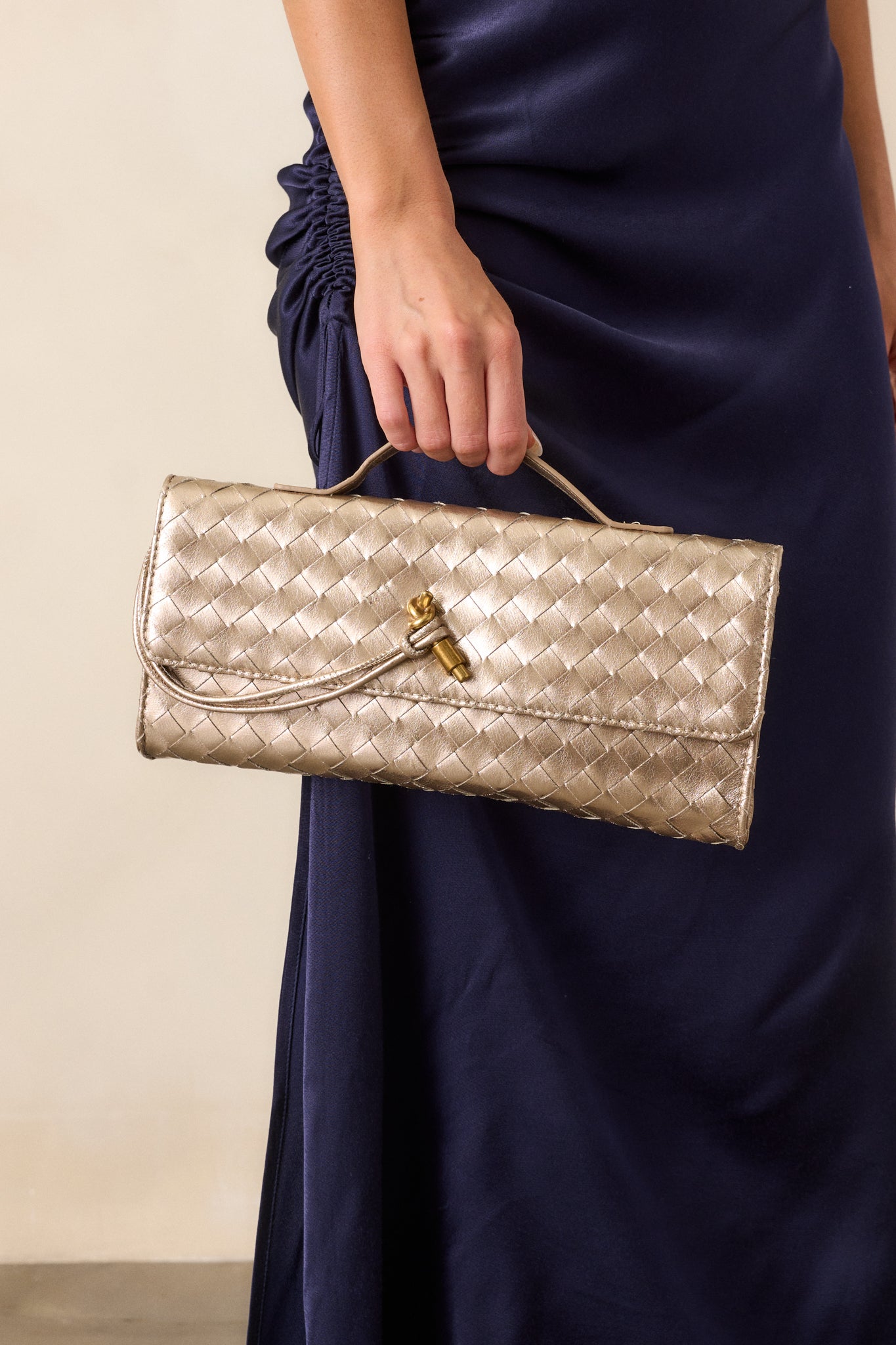 Full front view of the gold handbag, showcasing its rectangular shape, gold handle on top, and gold accent front piece with a magnetic fold-over closure.