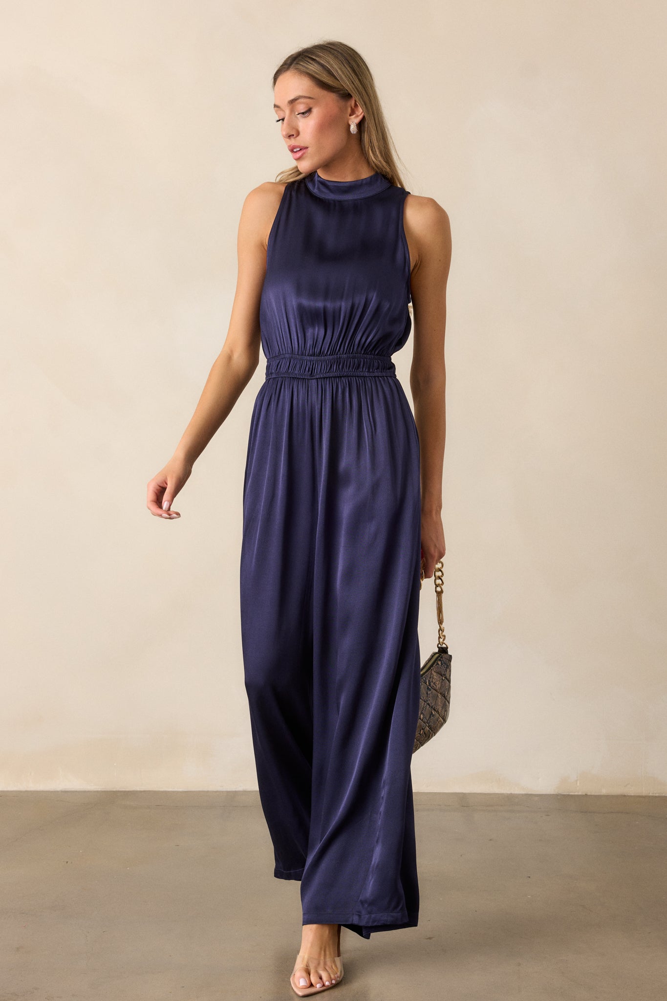 Angled front view of the jumpsuit, focusing on the high neckline, the smooth lines of the elastic cinch waist, and the long, flowy pant legs.