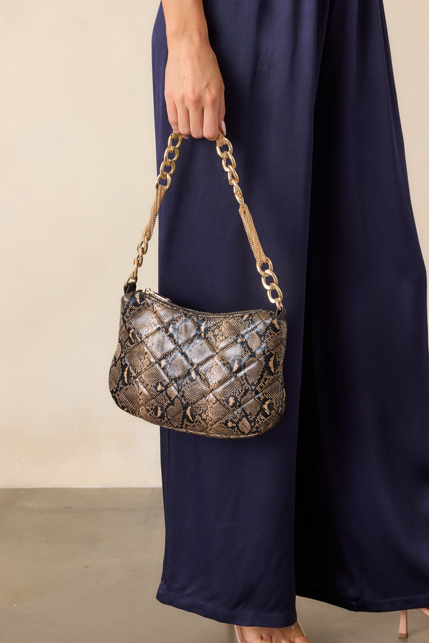 Full view of the snakeskin faux leather handbag, highlighting its quilted design, thick gold chain, and top zipper closure.