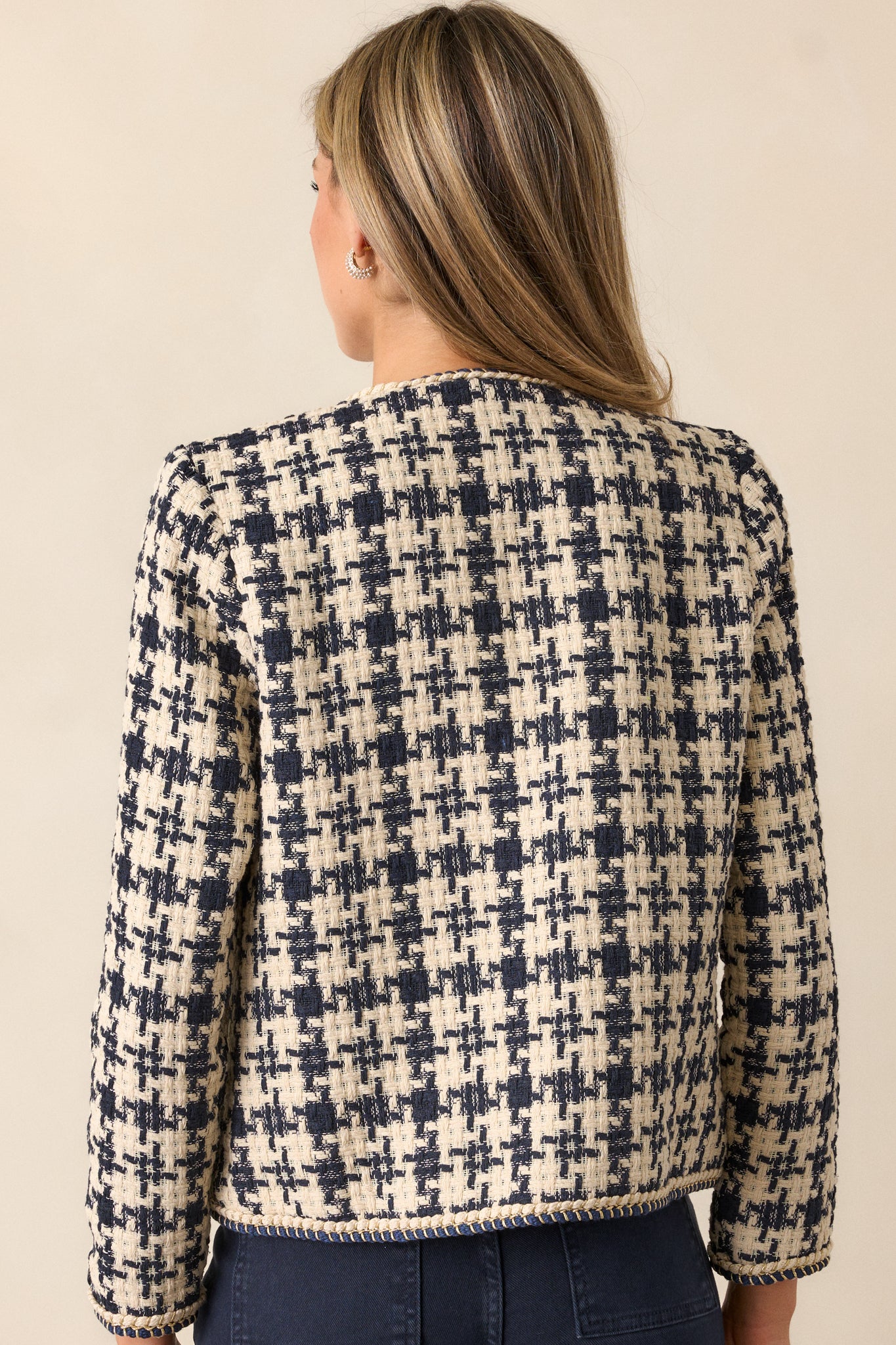 A back view of the navy tweed jacket, highlighting the clean lines and boxy fit. The houndstooth design continues on the back, with the gold rope twist detail visible along the edges.