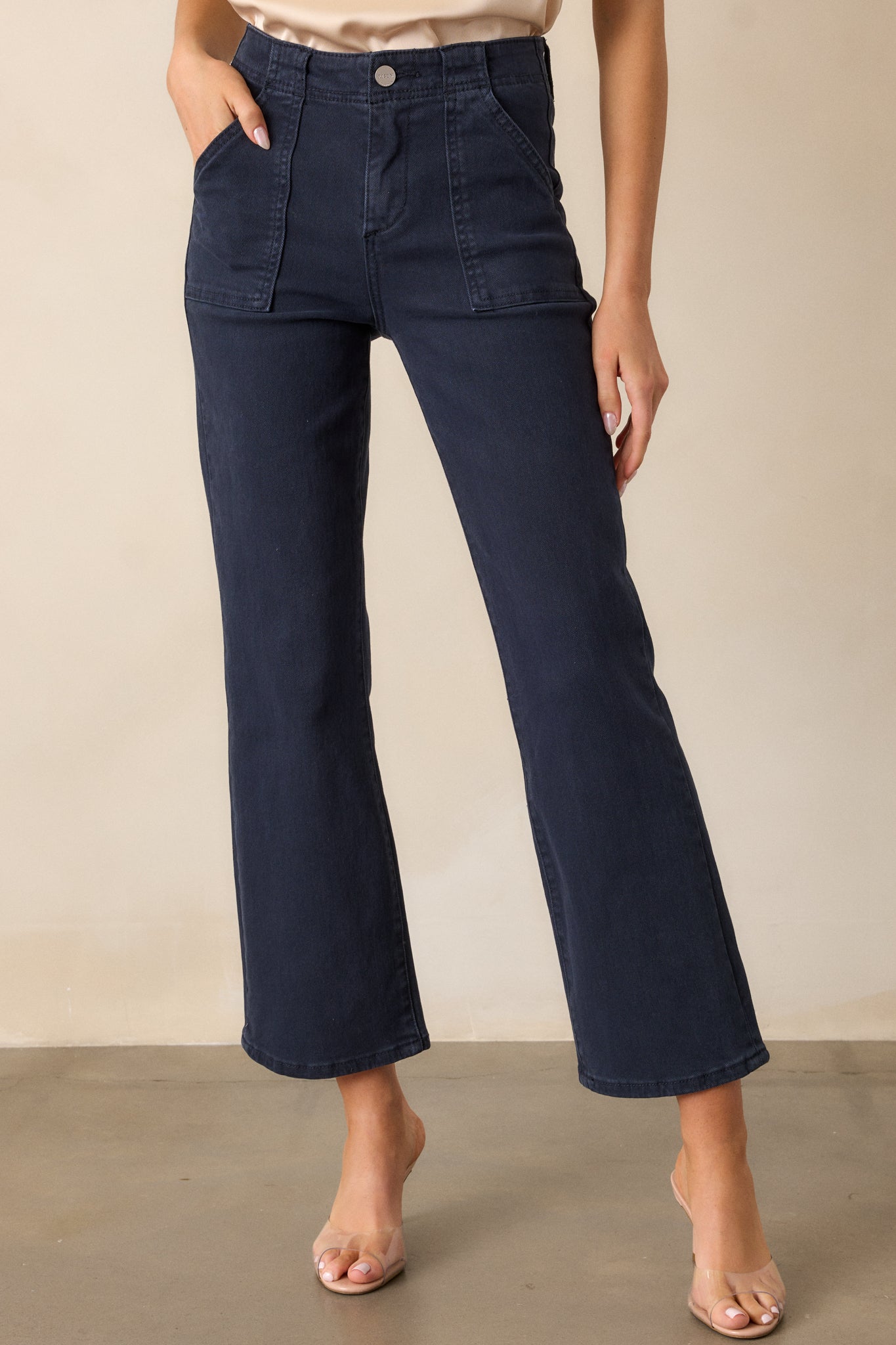 A cropped view of the navy jeans, highlighting the large front pockets and the button and zipper closure at the waist. The clean lines of the jeans are visible, emphasizing their high-waisted design.