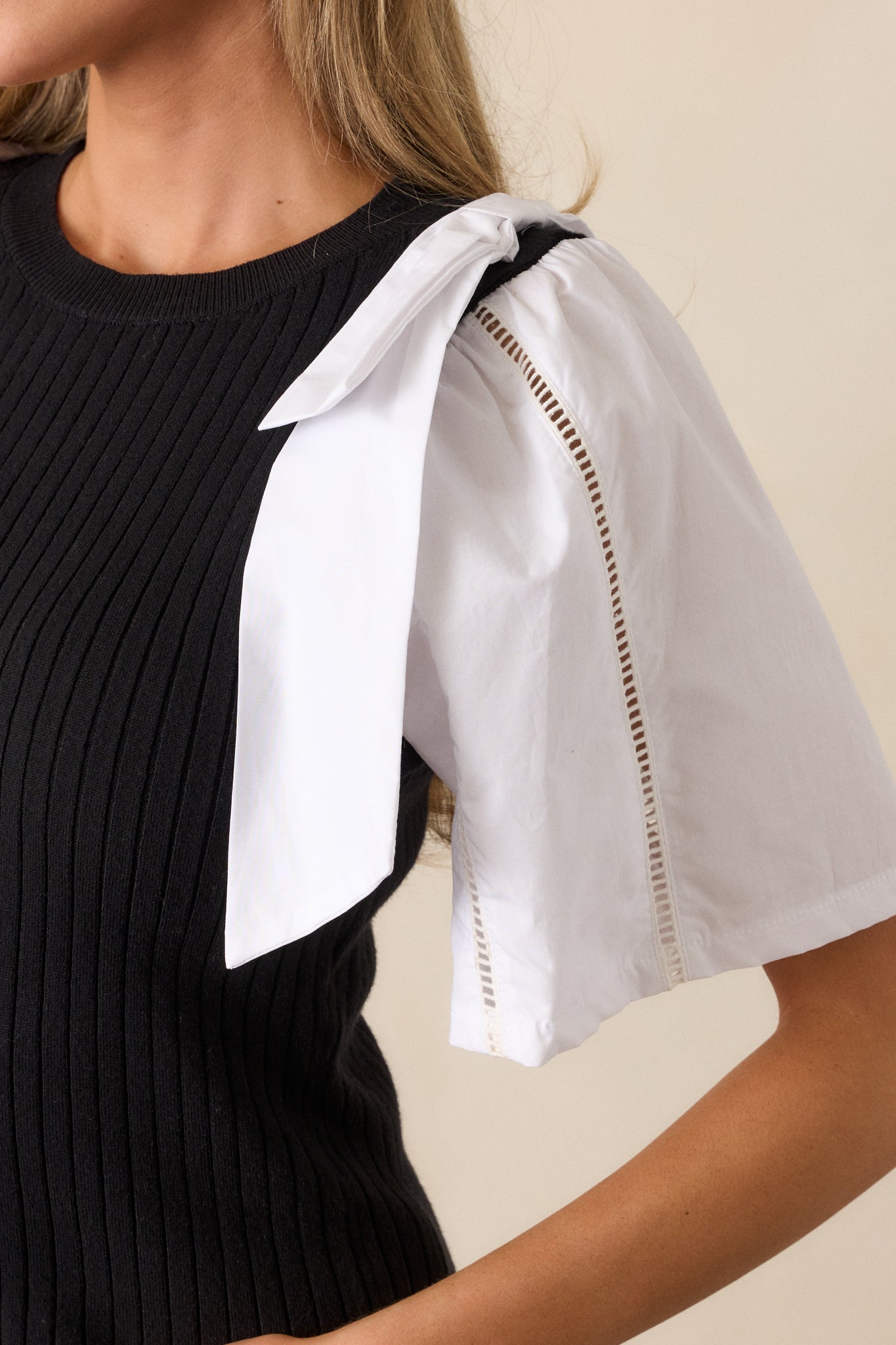 A close-up of one shoulder, capturing the bowtie detail on the black and white sweater top and the intricate cut-out design along the color-blocked sleeve.