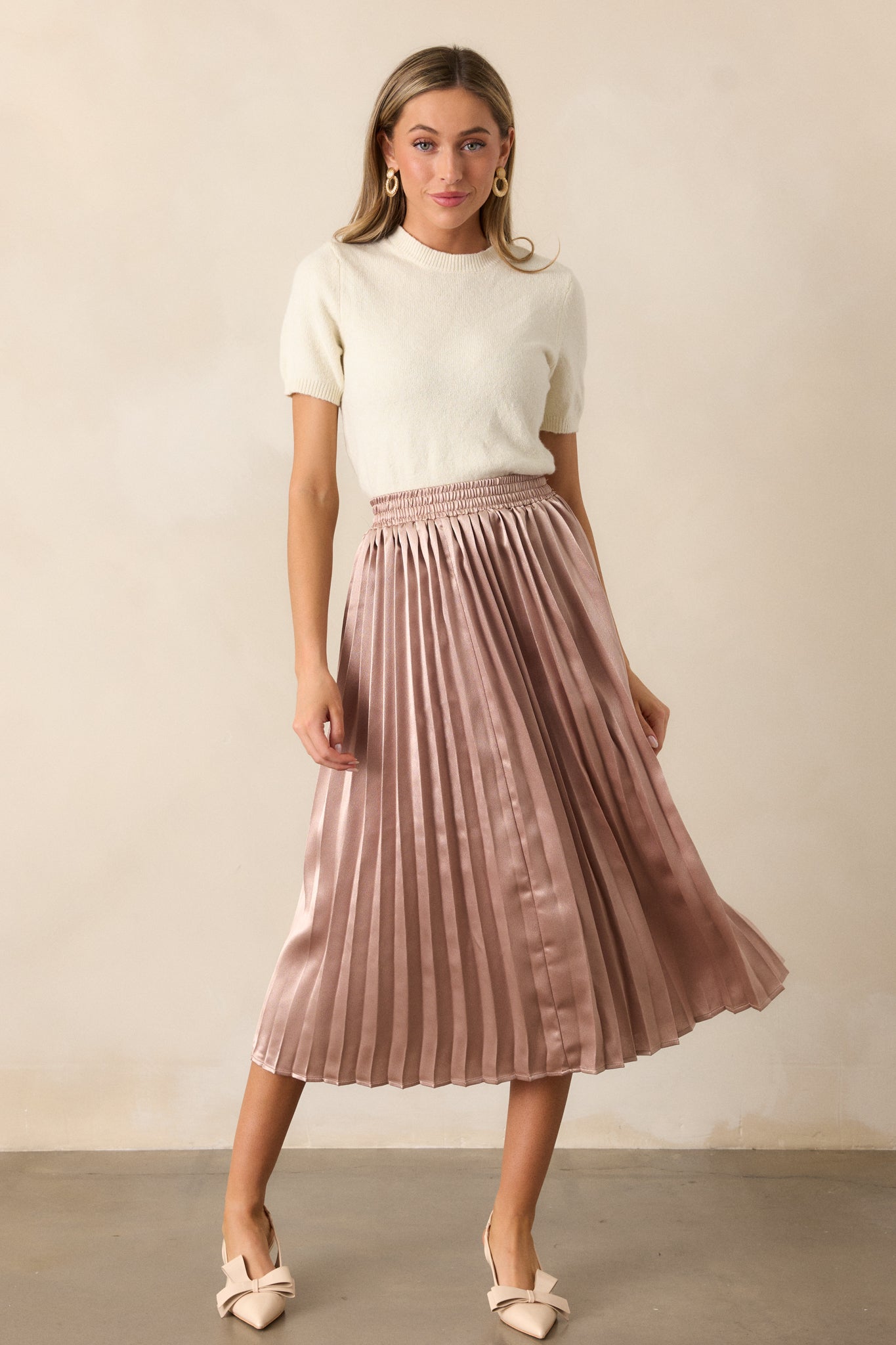 Another front view of the rose gold skirt, showcasing its pleated fabric, elastic waistband, and midi length, offering a graceful flow.