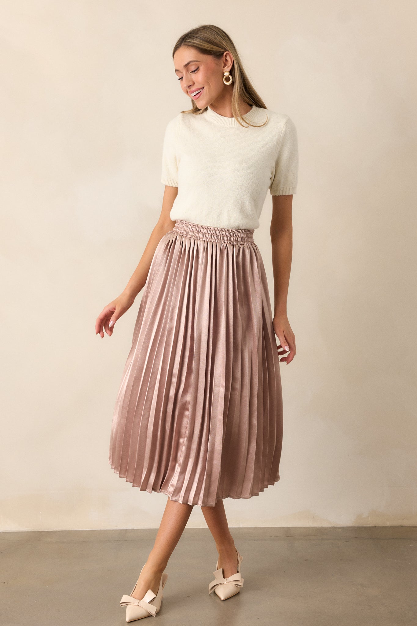 A full view of the rose gold skirt, showcasing its pleated fabric, elastic waistband, and midi length, offering a graceful flow.