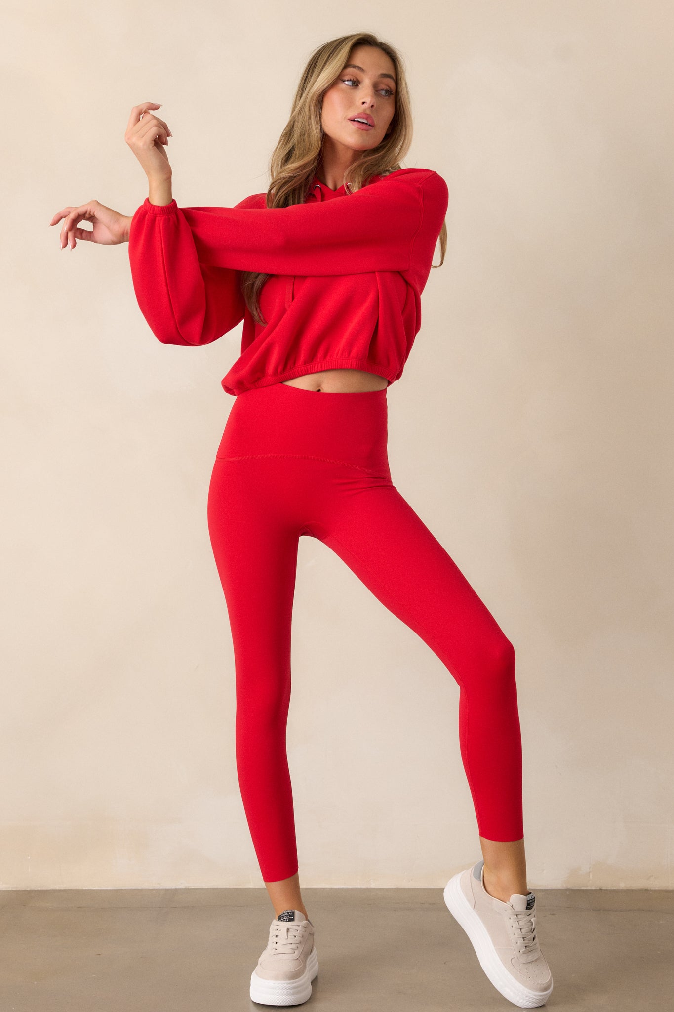 A full-body view of the red hoodie, emphasizing the slightly cropped silhouette, high neckline, and elastic cuffed sleeves. The elastic hem and draw cord add a sporty touch to the design.