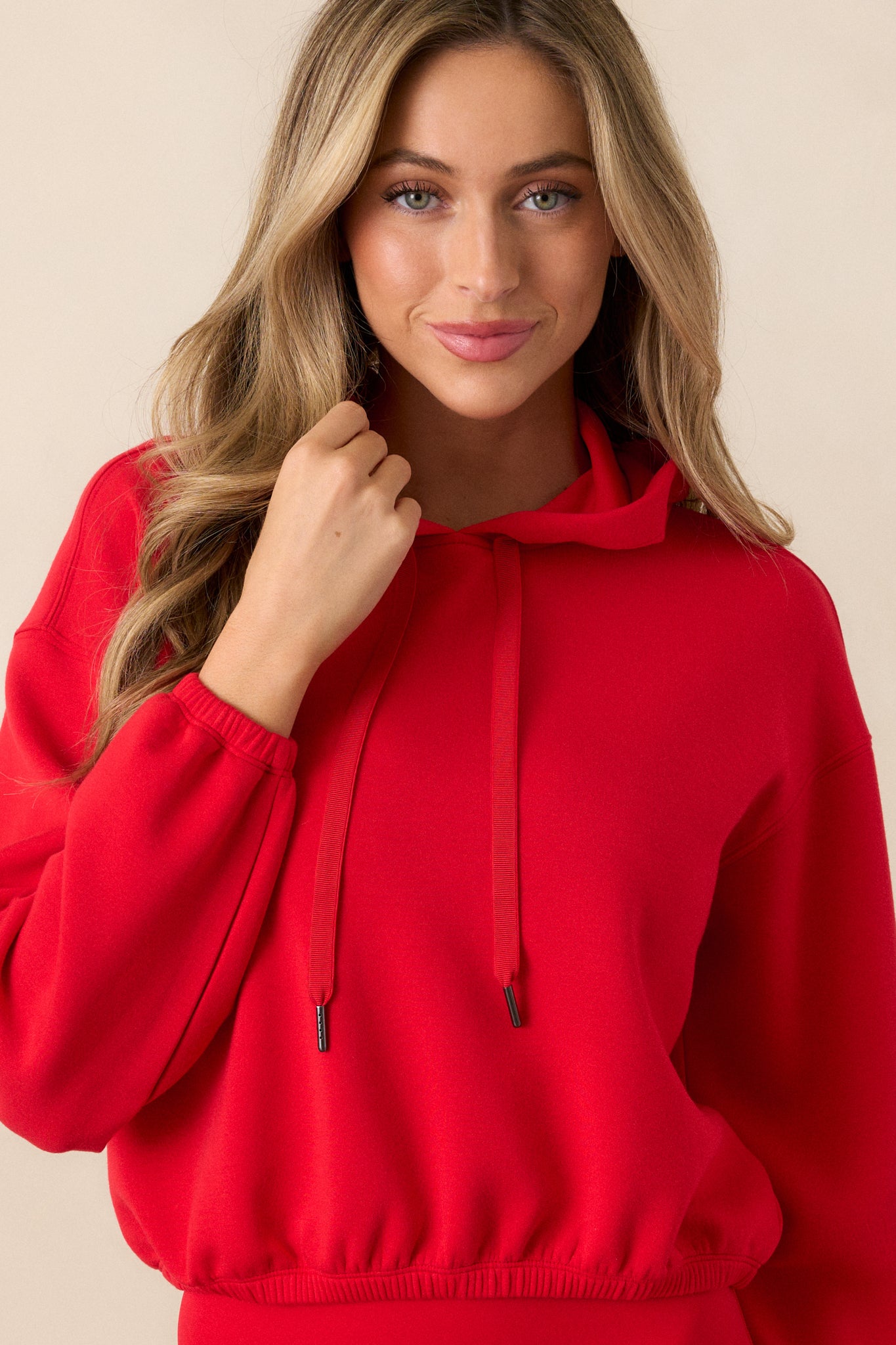 A close-cropped image focusing on the red hoodie’s high neckline, elastic cuffed sleeves, and the finely knit fabric. The draw cord is visible, enhancing the sporty look.