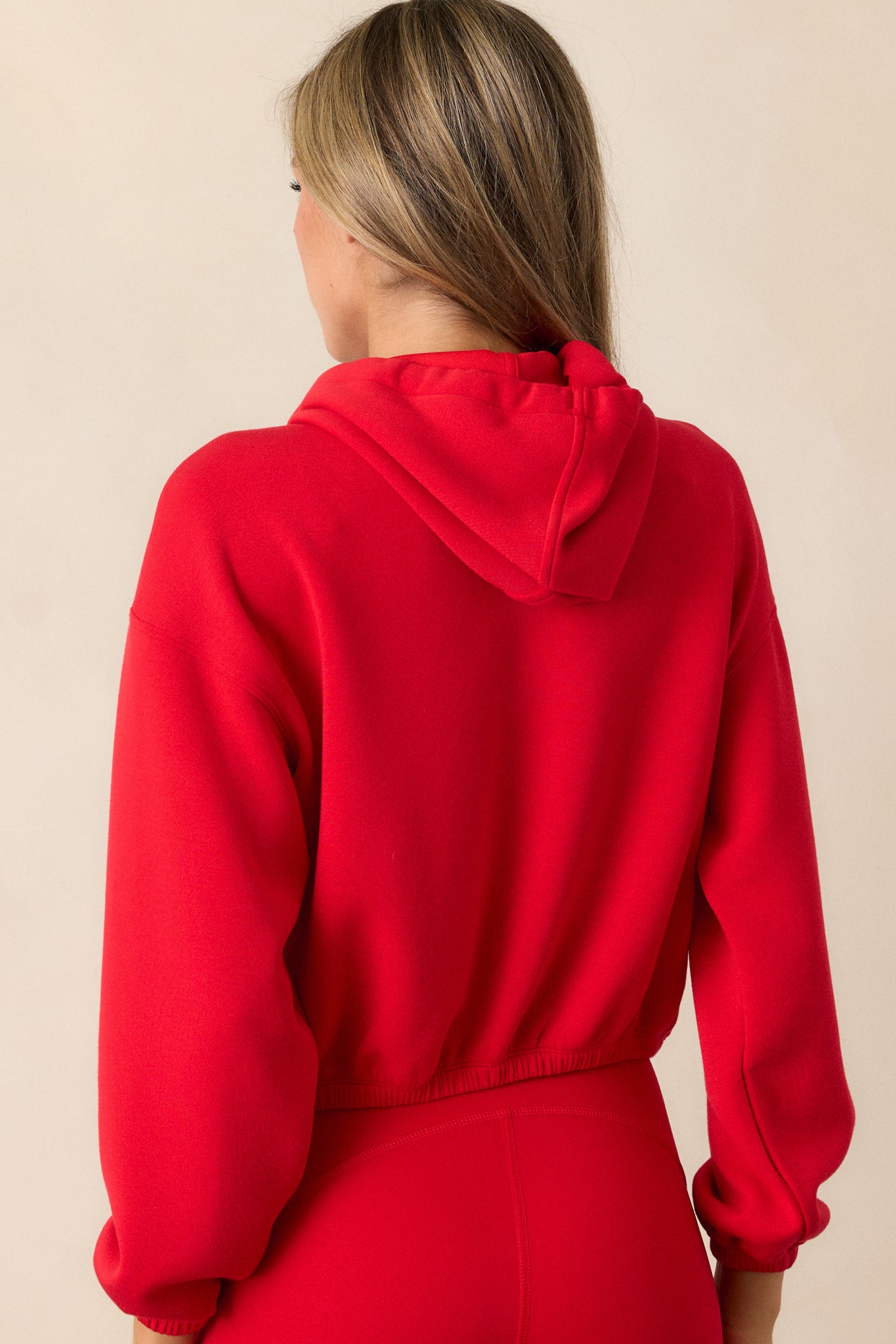 A back view of the red hoodie, showing the elastic hem and the slightly cropped fit. The high neckline and draw cord add an extra layer of style to the simple yet chic design.