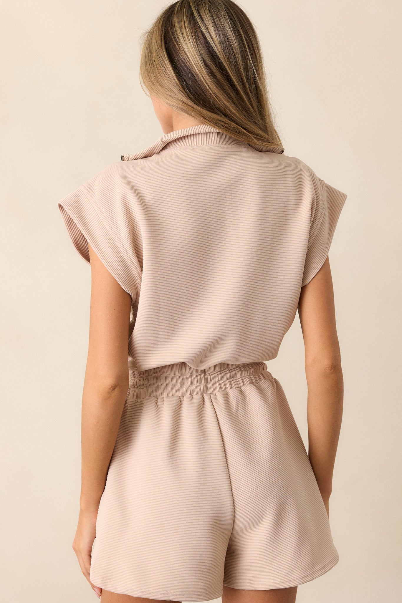 Back view of a taupe romper highlighting the overall fit, wide cap sleeves, and ribbed texture.