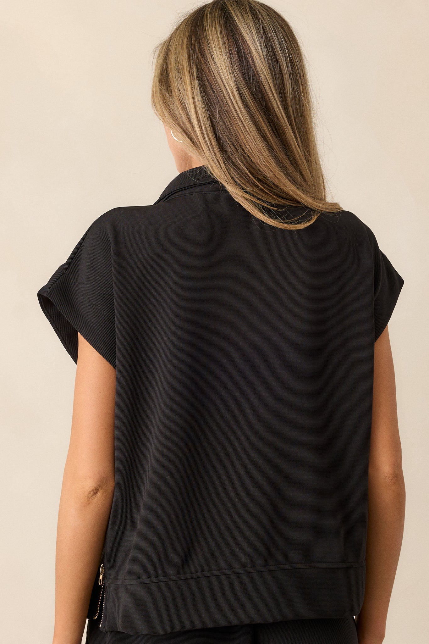 Back view of the black pullover, highlighting the simplicity of the back design, with short cap sleeves and the overall shape of the pullover. The zippers on the sides add an interesting design detail.