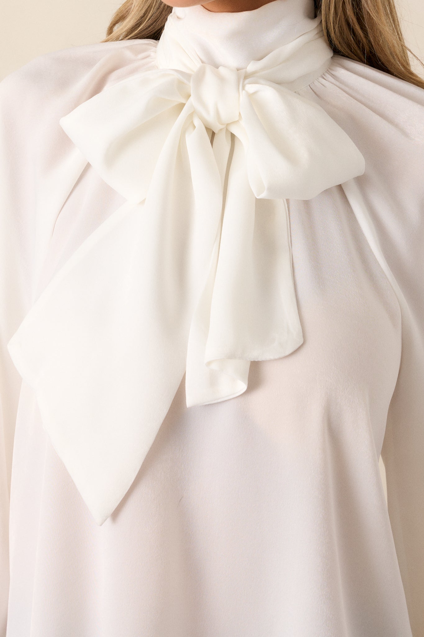 A close-up of the top’s high neckline, adjustable self-tie neck bow, and the relaxed, flowy fit of the white top.