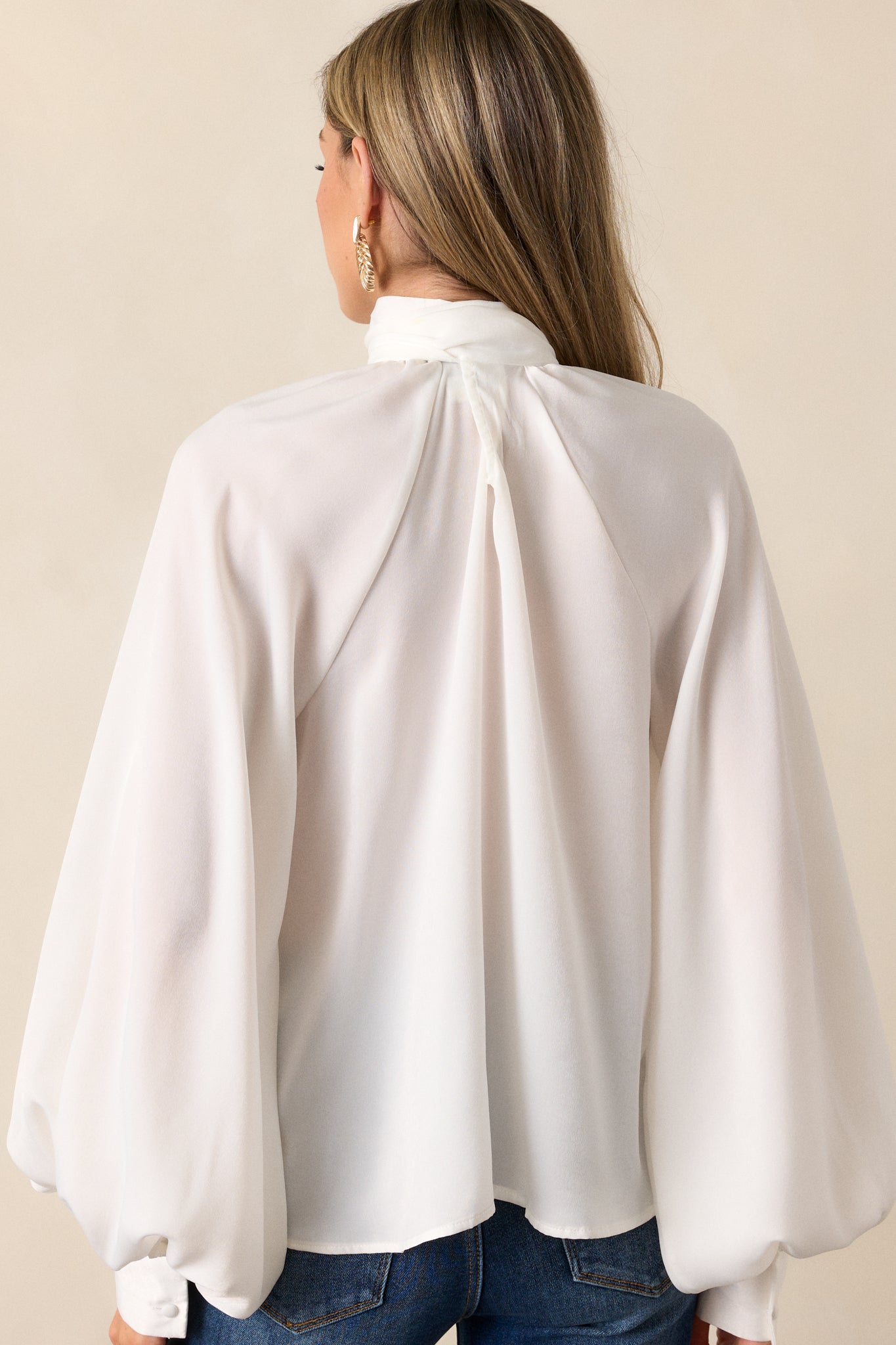 A view of the back of the white top with the self-tie styled as a bow in the front, highlighting the flowy fit and smooth fabric from behind.