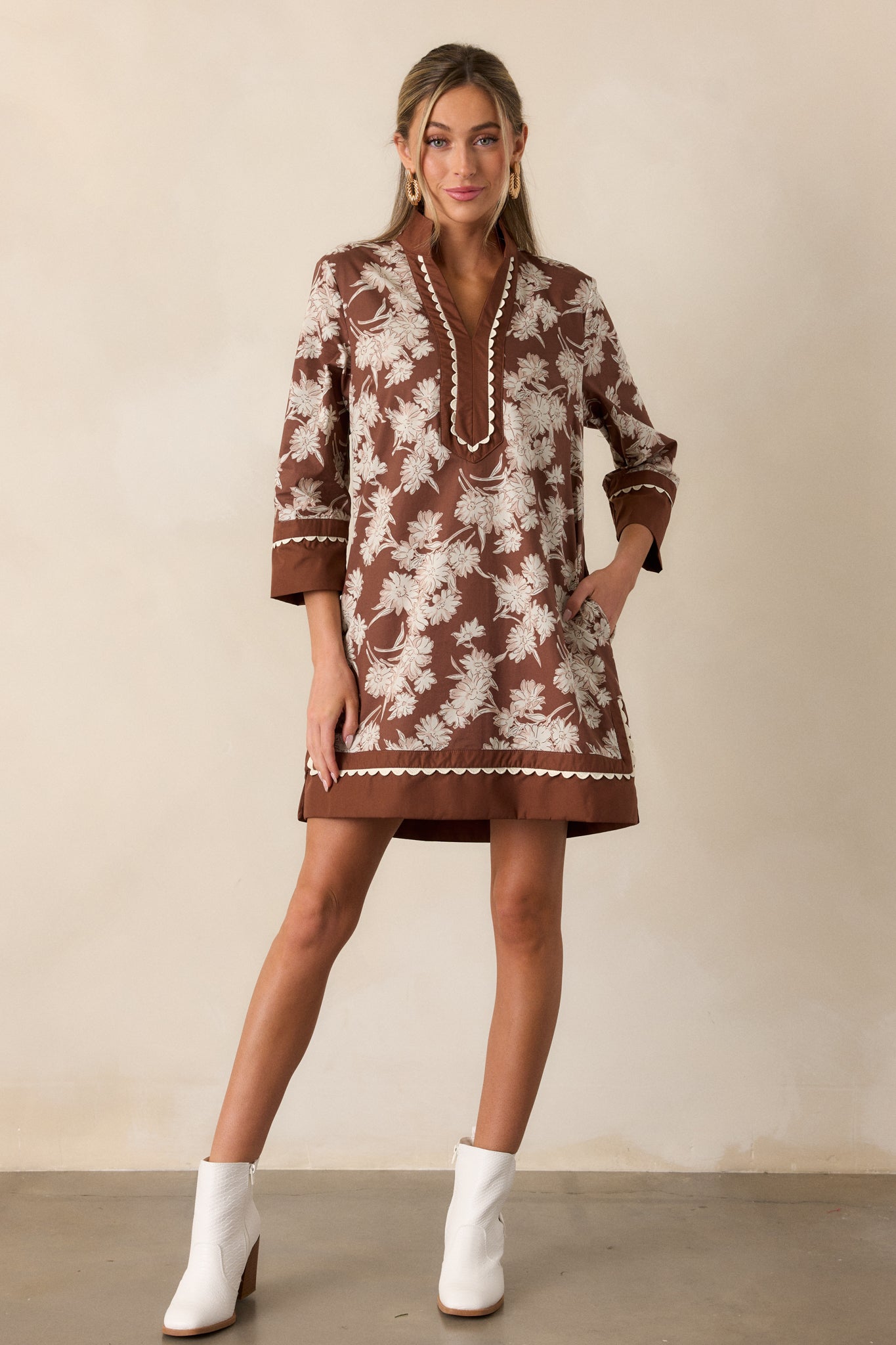 Chocolate dress with a v-neckline and white scalloped trim, highlighting the ivory floral detailing and long sleeves with wide cuffs at the wrists.