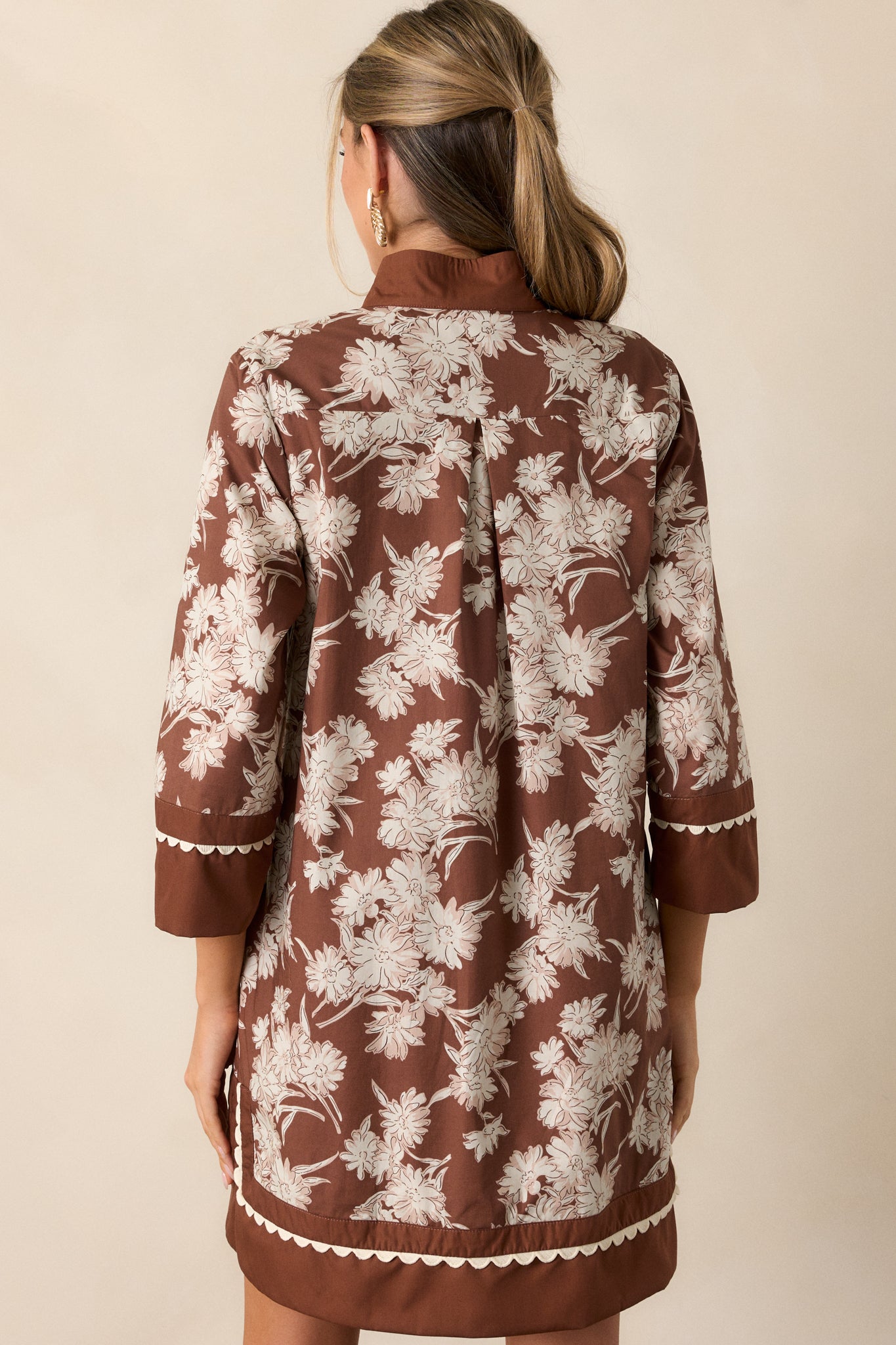 Back view of the chocolate mini dress, featuring long sleeves with wide cuffs and the smooth finish of the dress without the floral detailing visible.