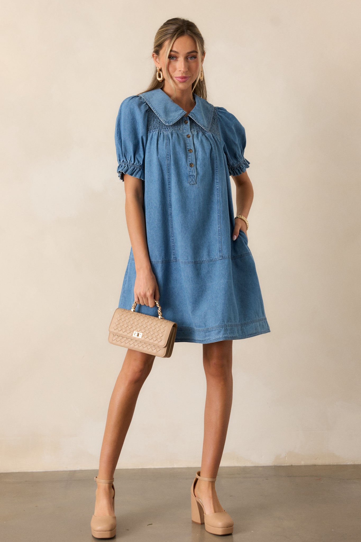 Medium wash denim dress with a peter pan collar, functional button front, and smocked yolk detailing, emphasizing the puff sleeves and elastic ruffle cuffs.