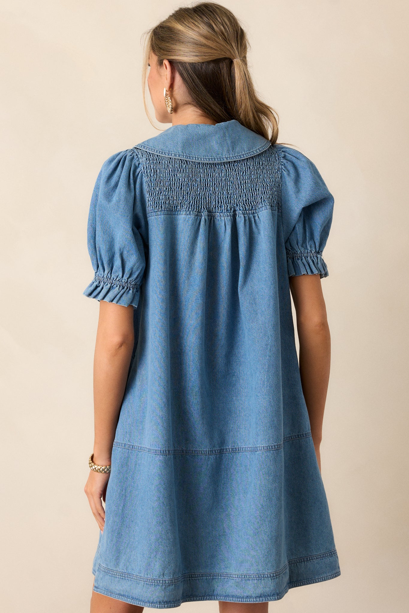 Back view of the denim dress, showing the puff sleeves, smocked yolk detailing, and the shift style silhouette.