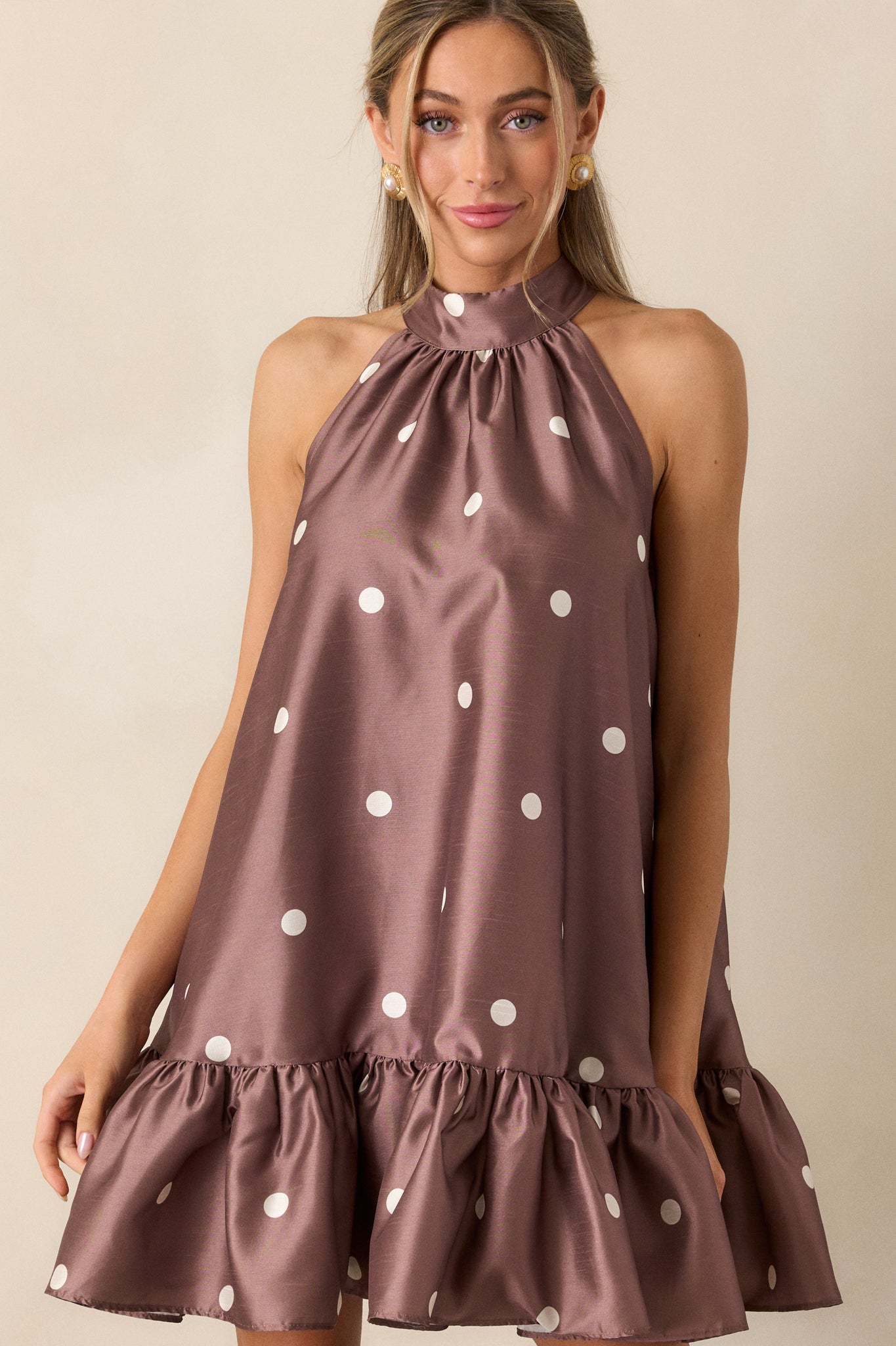 Another full-body view of the brown mini dress, highlighting the sleeveless design and the mini length. The ruffled hem and halter neckline with button clasps are clearly visible.