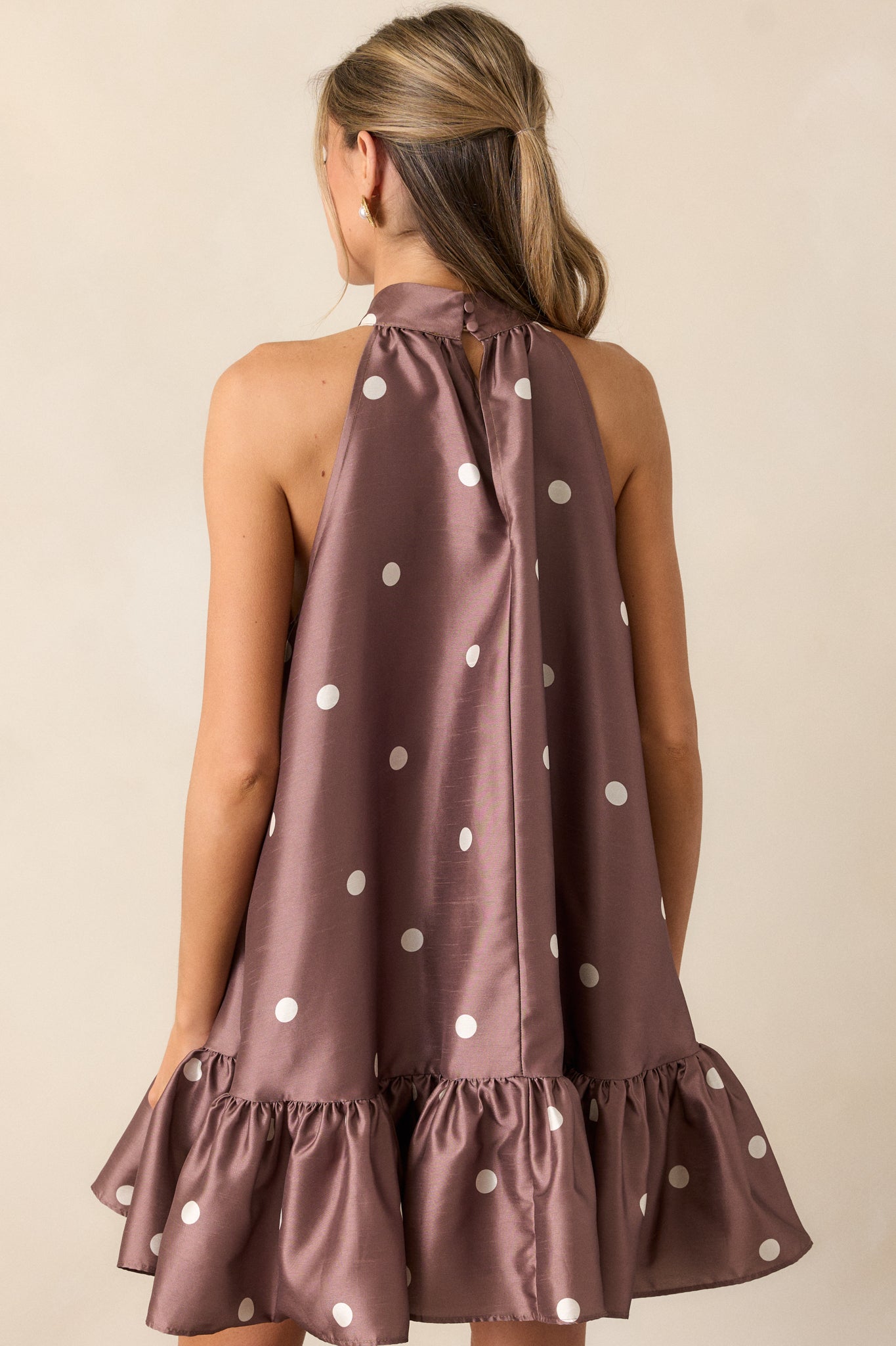 A back view of the dress, focusing on the halter neckline with button clasps and the overall flow of the fabric. The ruffle bottom hem and mini length are visible from this angle.