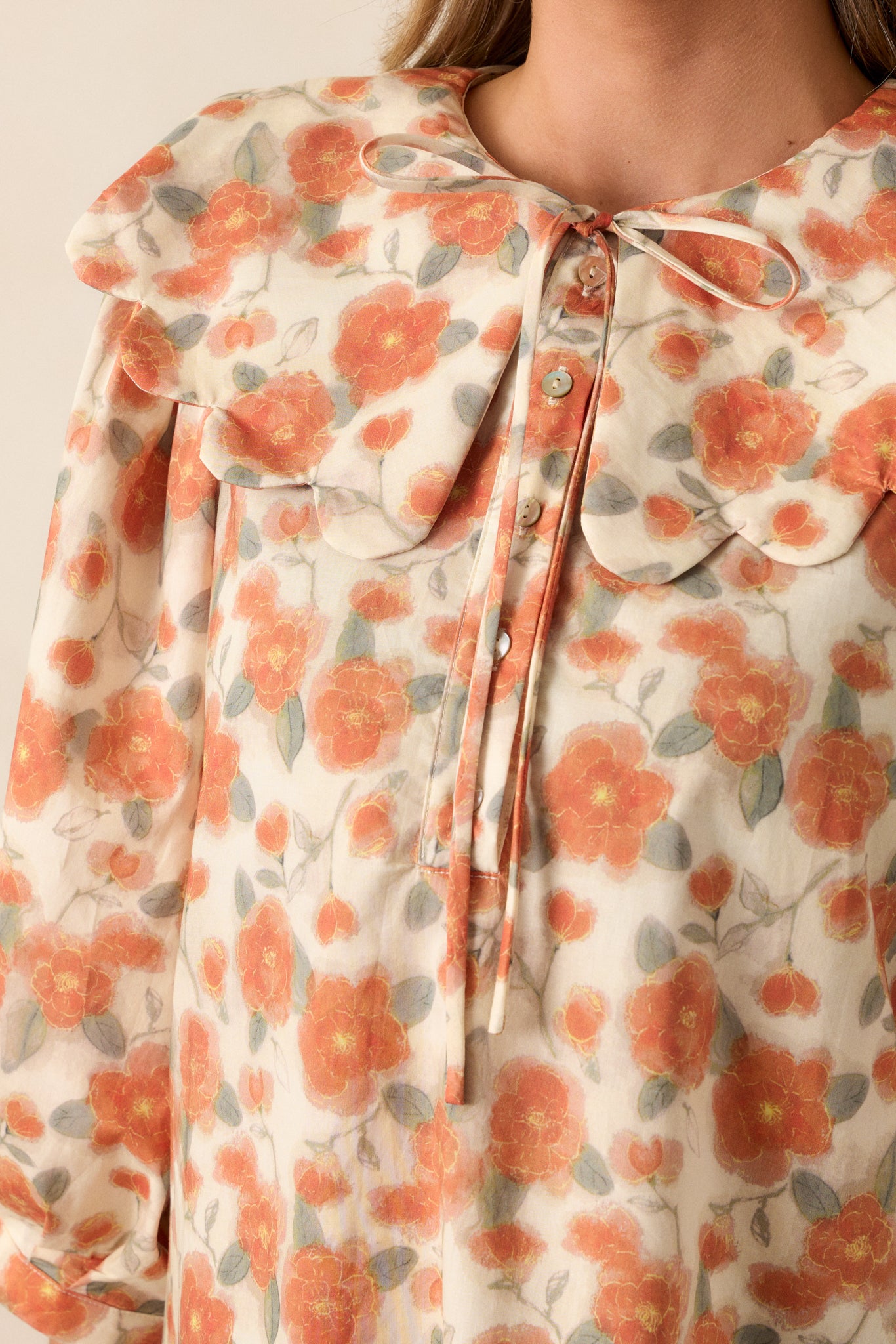 Close-up of the self-tie detail at the peter pan collar, showcasing the apricot blouse’s floral pattern up close.