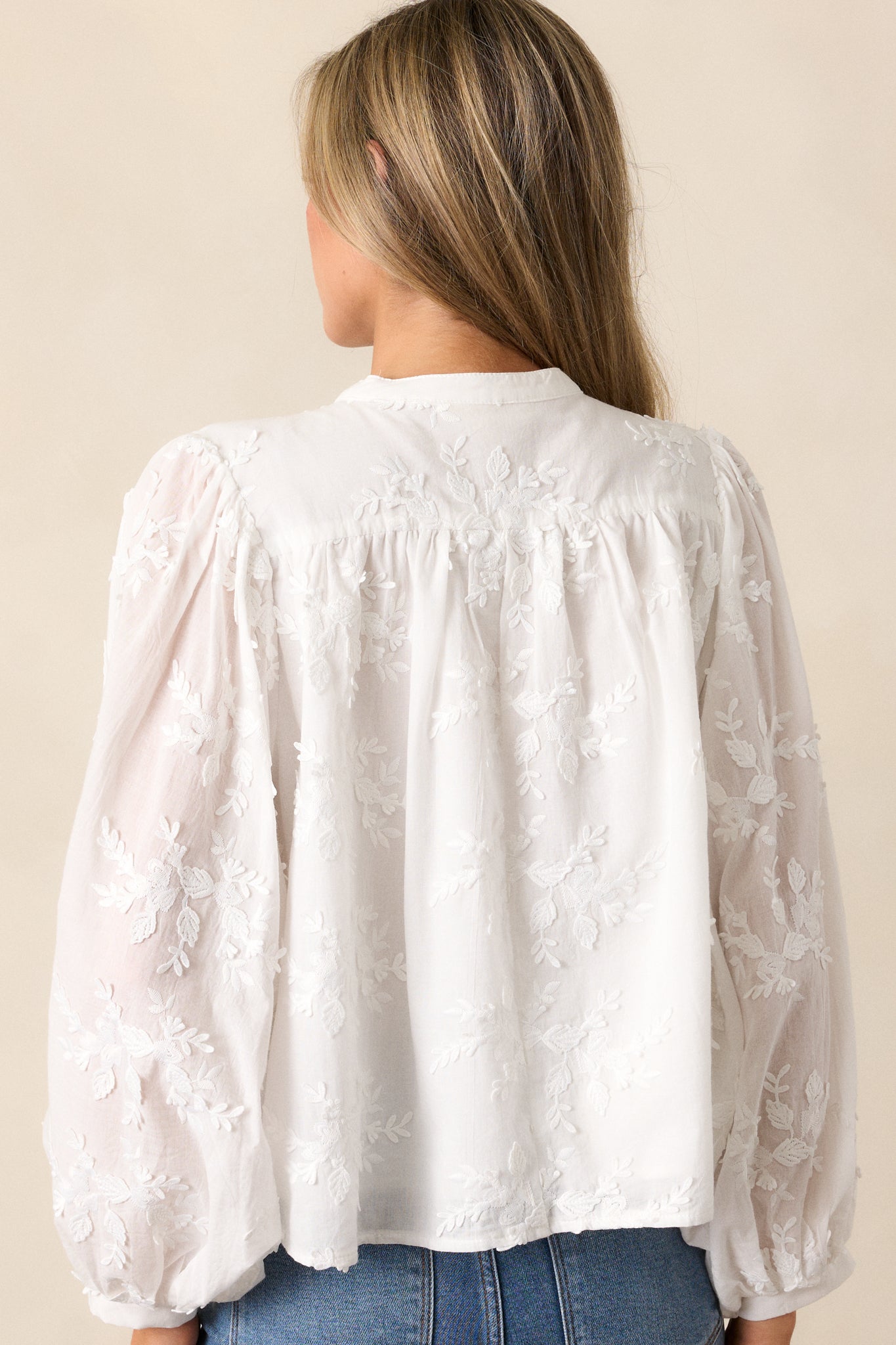 Back view of the white blouse with a high rounded neckline, showing the long sleeves and continuous textured floral design.