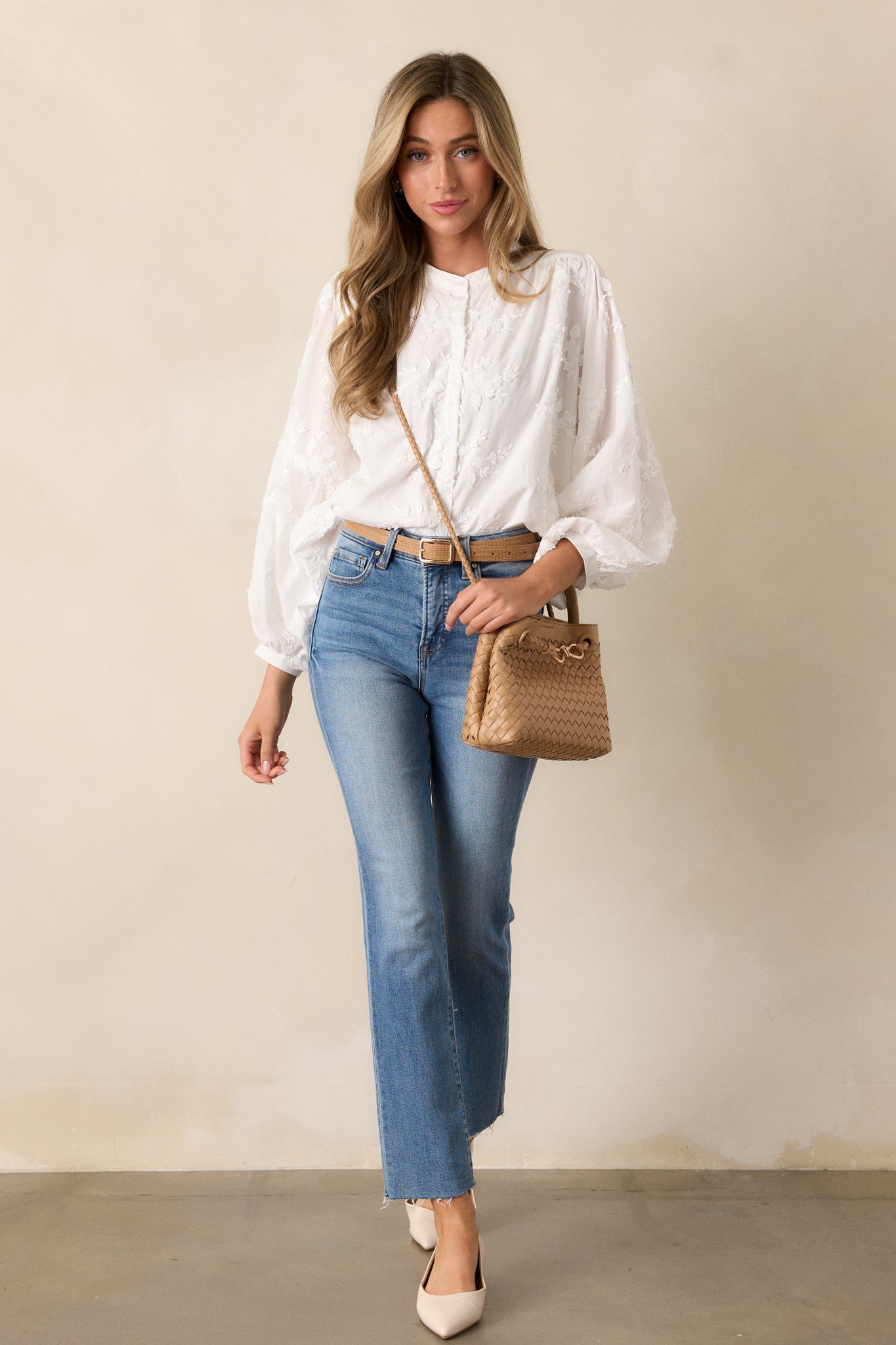 White blouse with a button front and high rounded neckline, highlighting the long sleeves and delicate textured floral pattern.